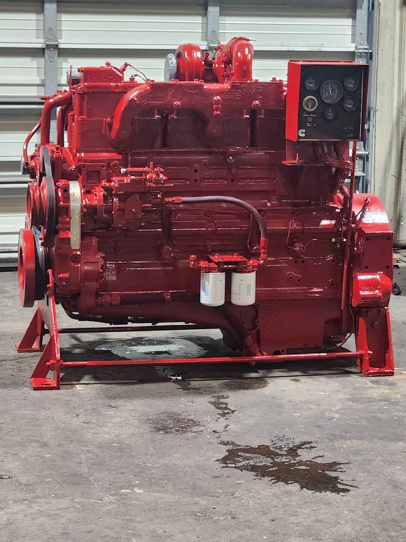 Red industrial engine painted bright red, mounted on a stand in a workshop with a control panel. | S&V Diesel Repair