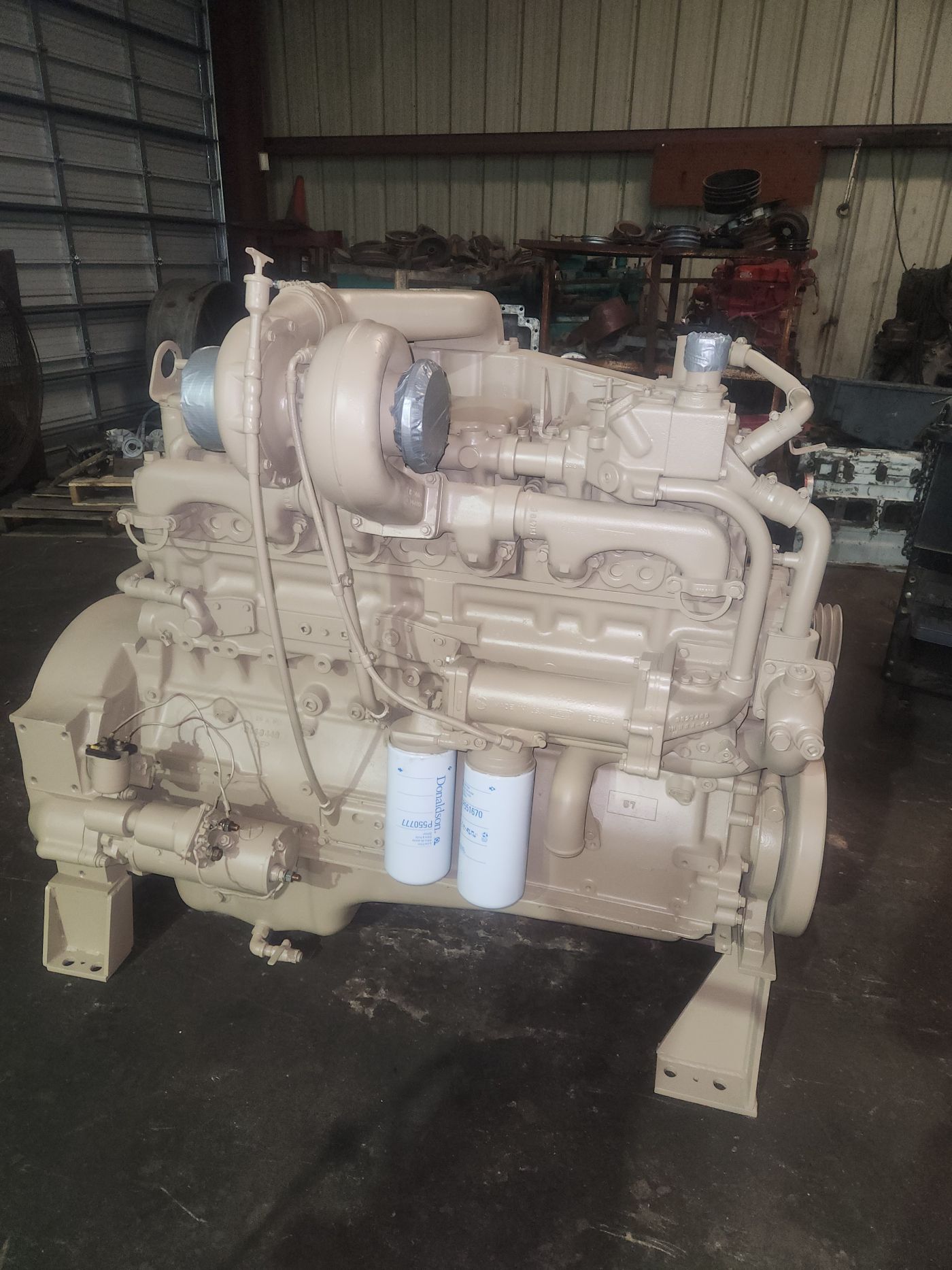 Large beige industrial engine mounted on a stand inside a workshop, with pipes and filters visible. | S&V Diesel Repair