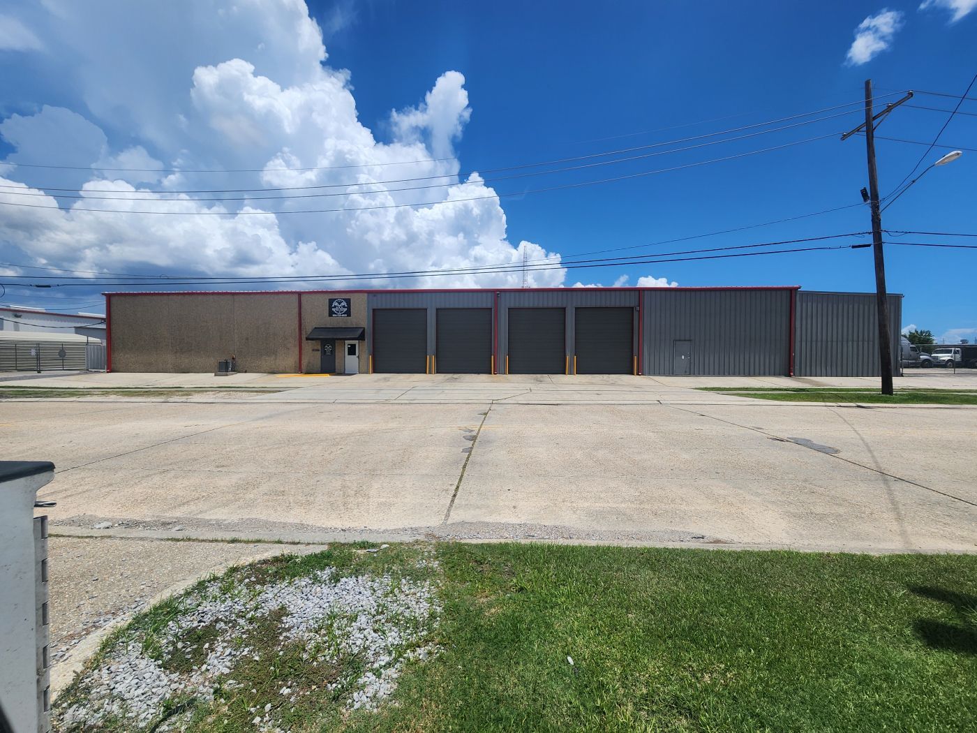 Single-story industrial building with a tan facade, parking lot, and bright blue sky with clouds. | S&V Diesel Repair