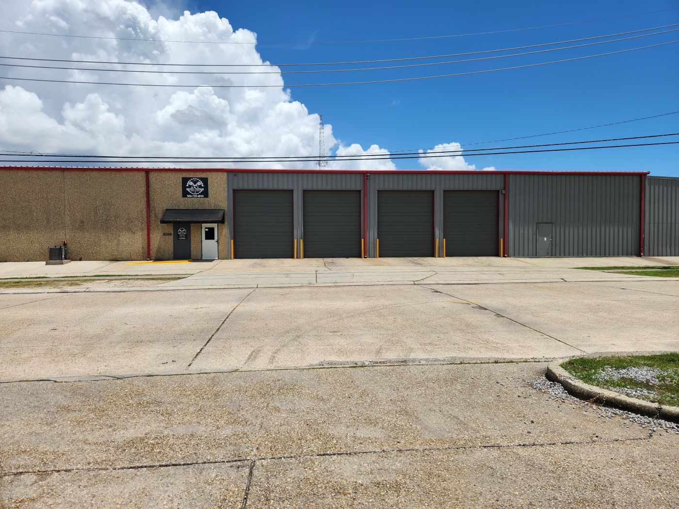 Empty industrial building with three garage doors and a small entrance under a bright blue sky | S&V Diesel Repair