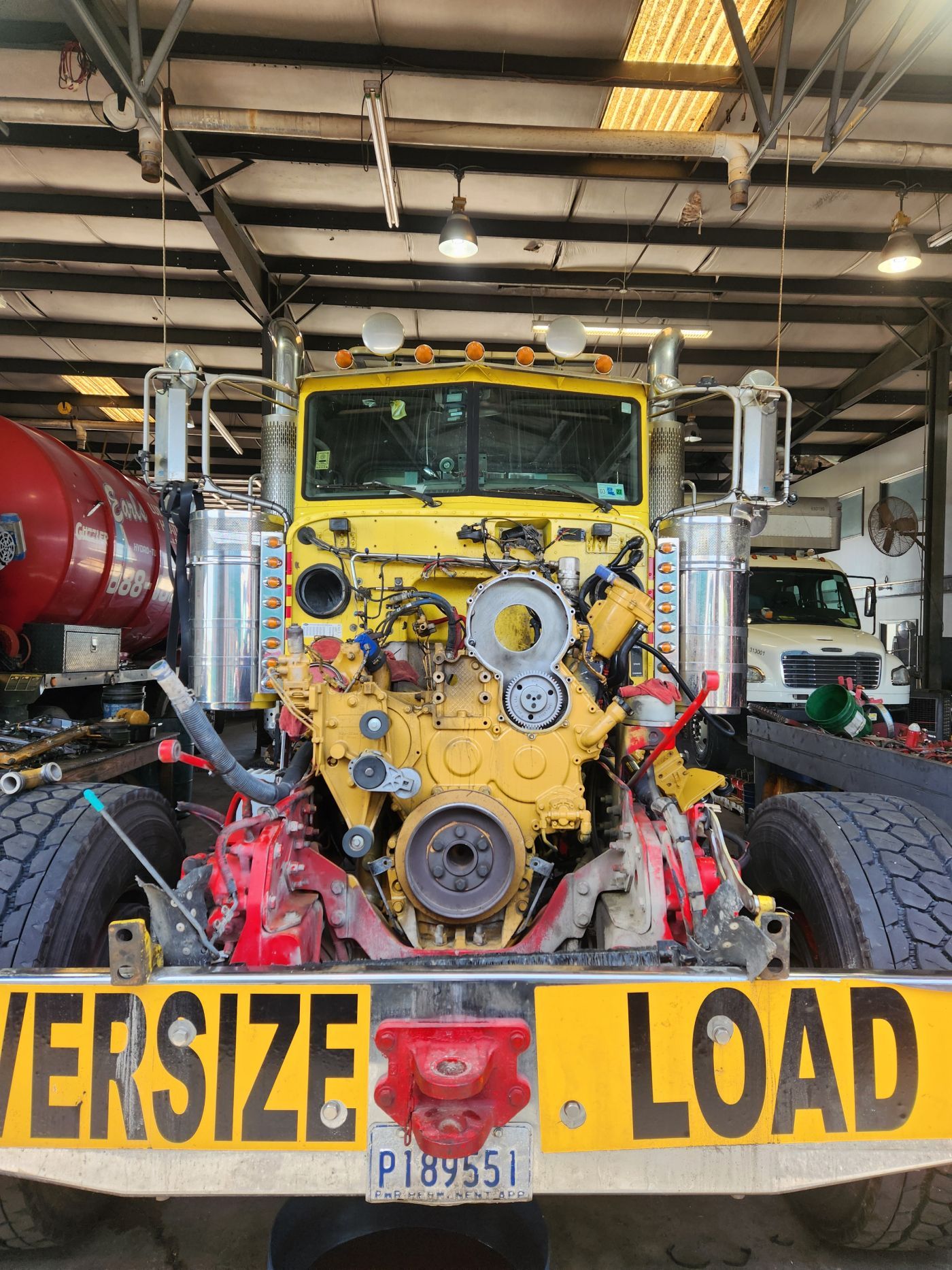 Yellow off-road truck in a garage, front view, with oversized load sign. | S&V Diesel Repair