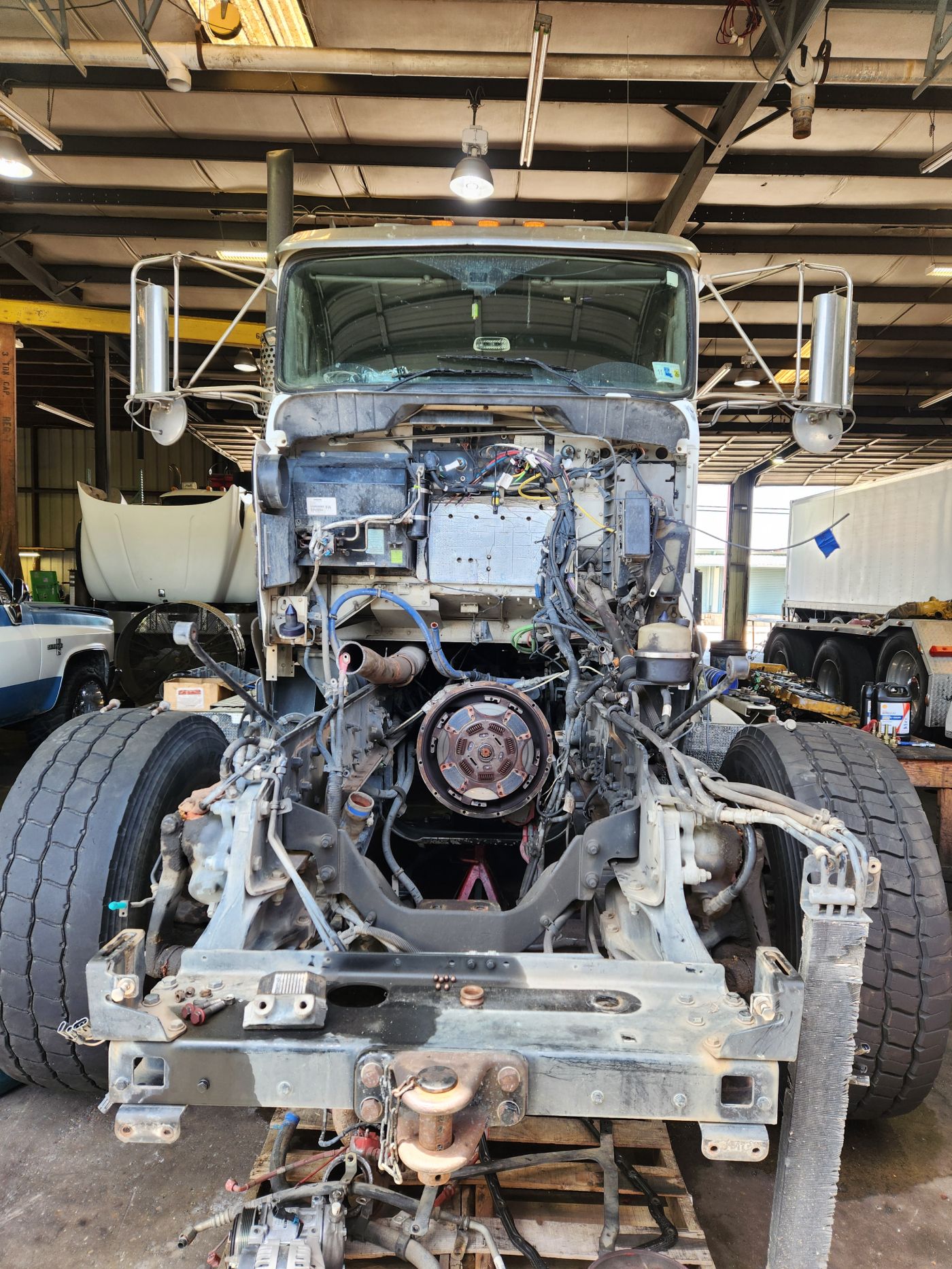 Front view of a stripped truck chassis in a workshop, with engine exposed and front wheels attached | S&V Diesel Repair
