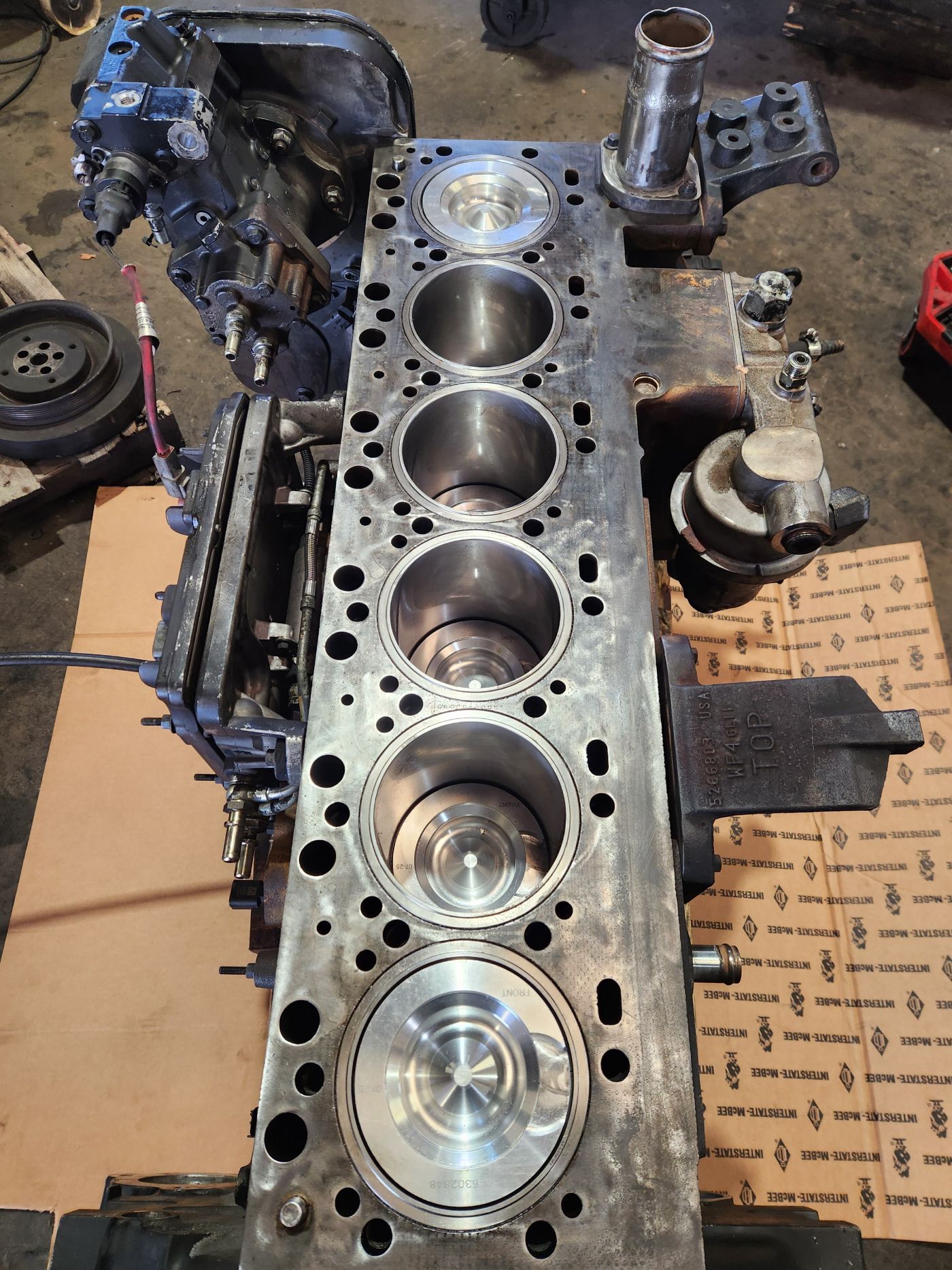 Disassembled engine block with exposed pistons and cylinder head parts on cardboard in a workshop. | S&V Diesel Repair