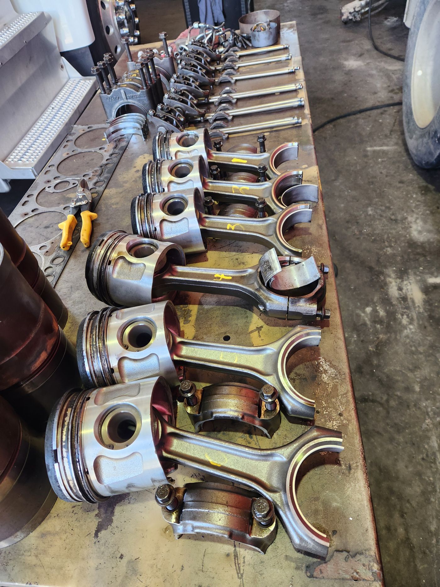 Row of disassembled engine pistons and connecting rods laid out on a workshop floor | S&V Diesel Repair