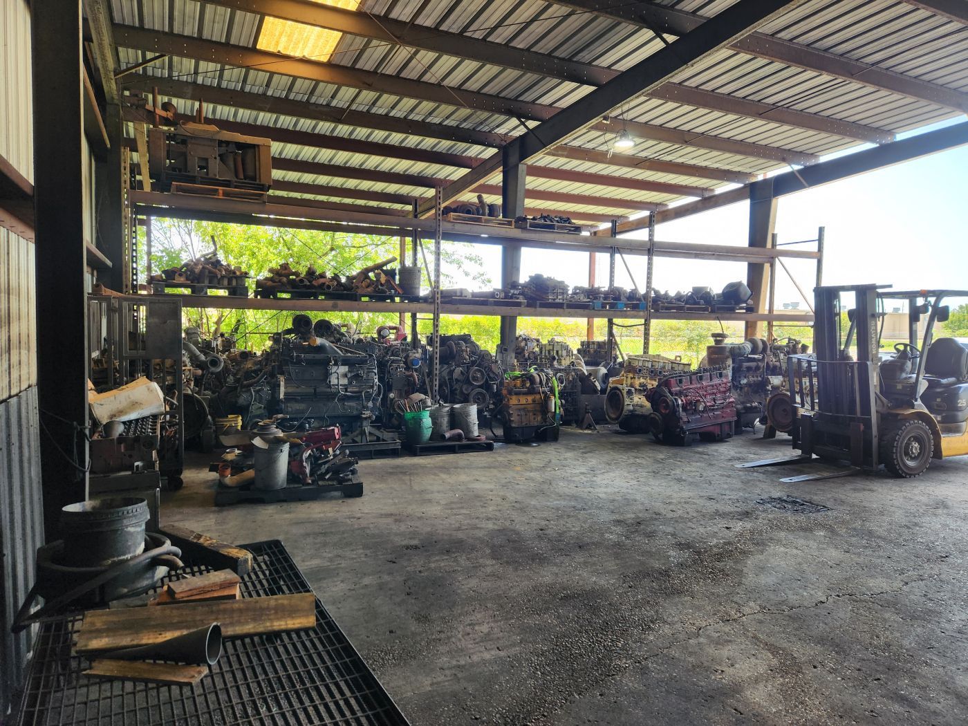 Open-sided warehouse with stacked farm equipment and a forklift on a concrete floor. | S&V Diesel Repair