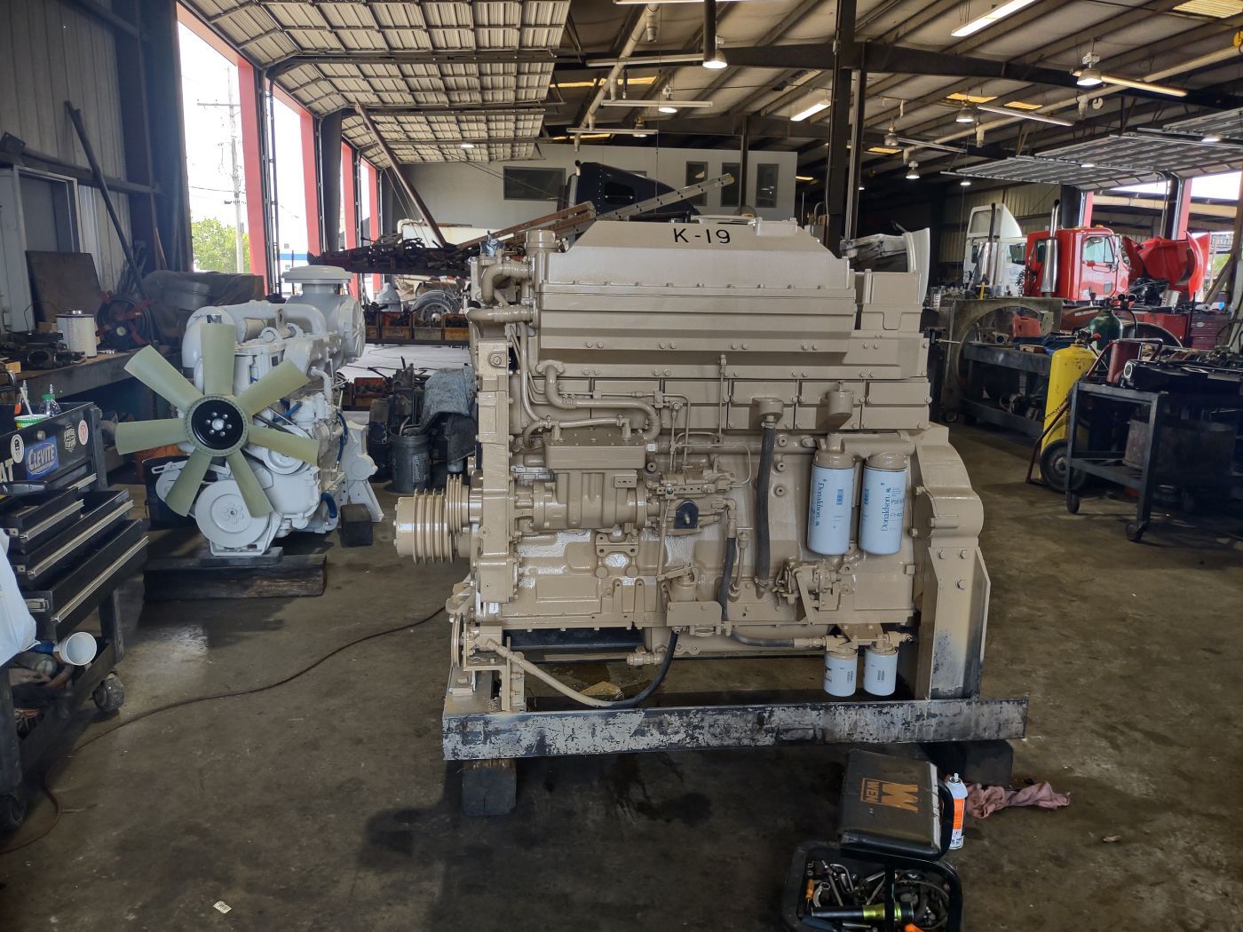 Large tan industrial engine or generator in a workshop with tools and equipment around it | S&V Diesel Repair