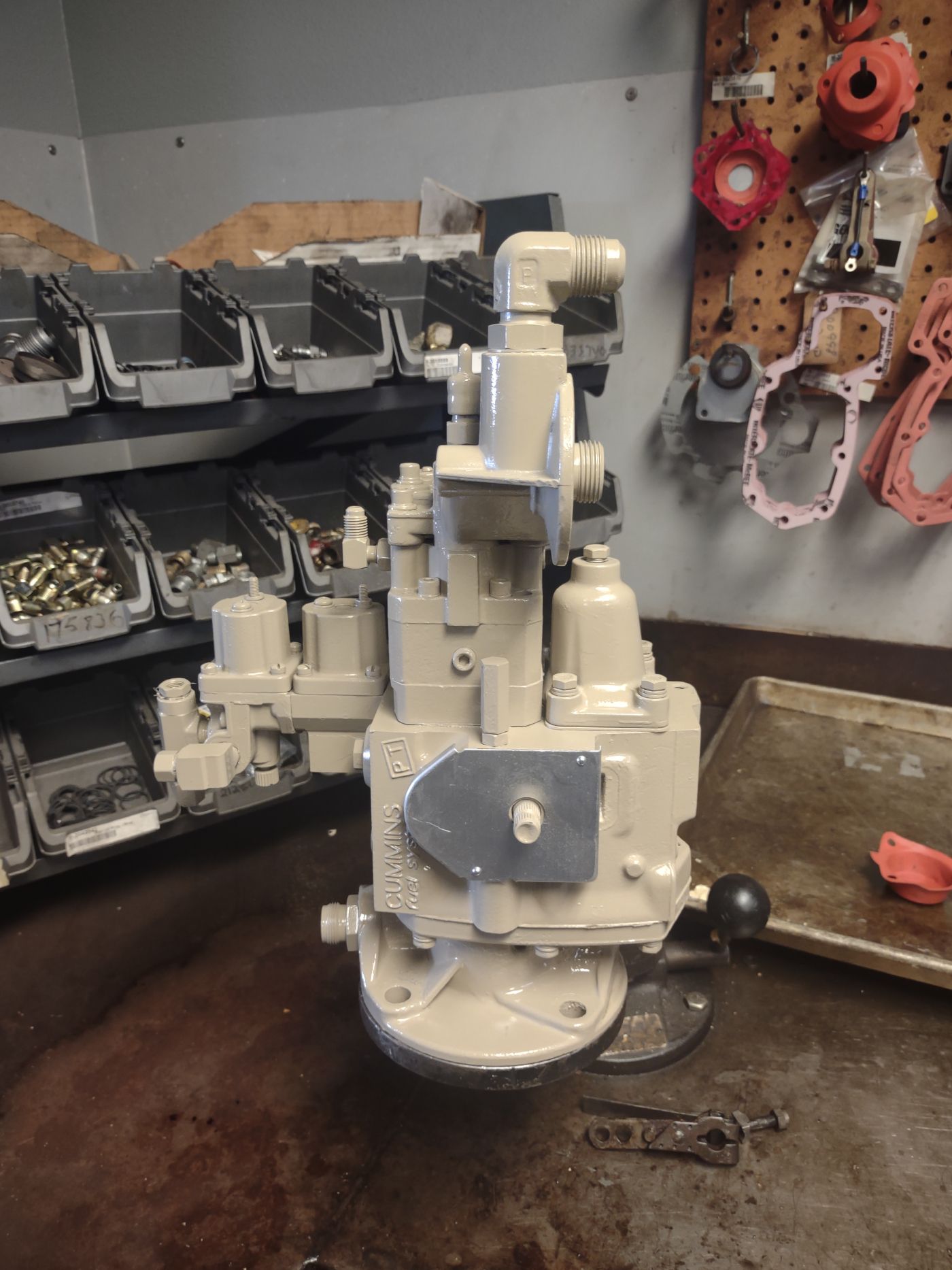 Beige industrial valve assembly on a workbench in a workshop, with shelves of metal parts behind it | S&V Diesel Repair