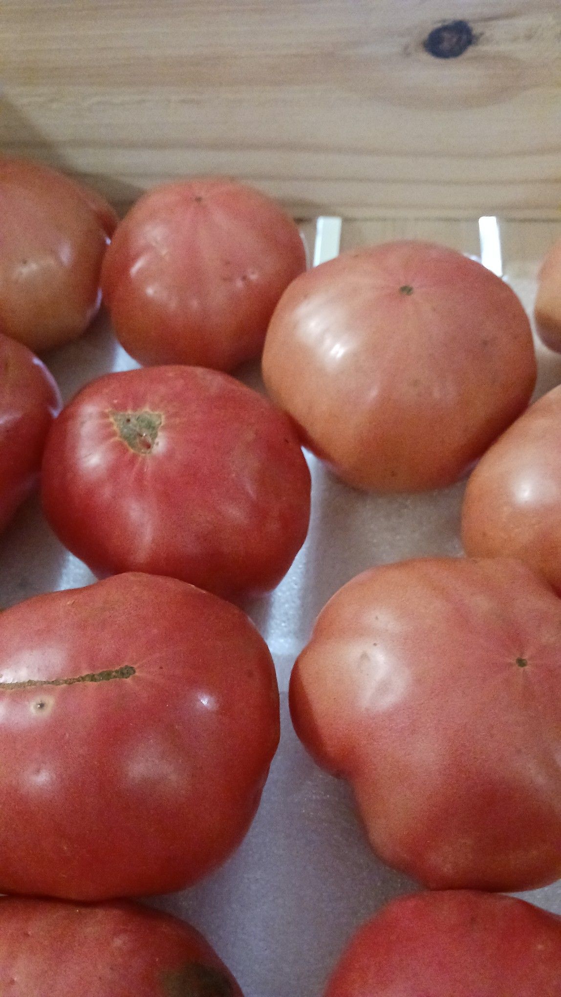 Pink-red tomatoes piled in a wooden crate, possibly for sale.