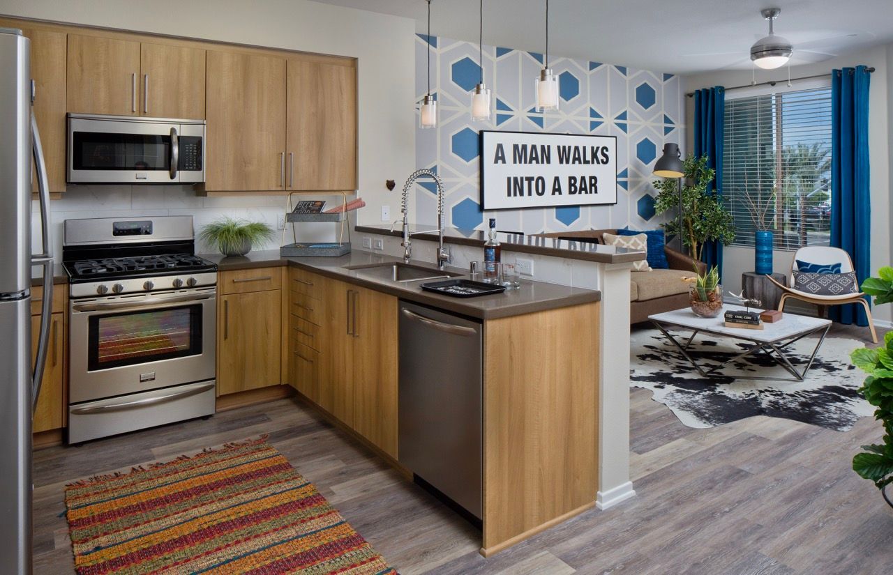 Open-concept kitchen and living area with wood cabinets, stainless appliances, and geometric blue wallpaper.
