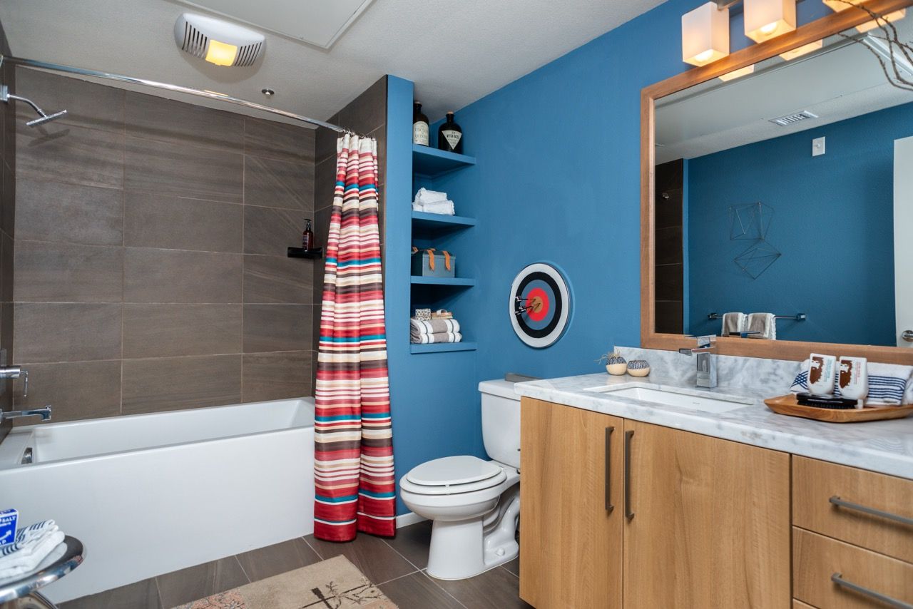 Blue bathroom with a wooden vanity, marble countertop, toilet, and striped shower curtain.