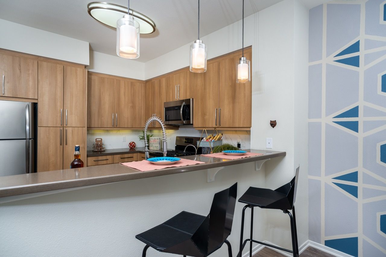 Modern apartment kitchen with wood cabinets, stainless steel appliances, and a bar-height counter.