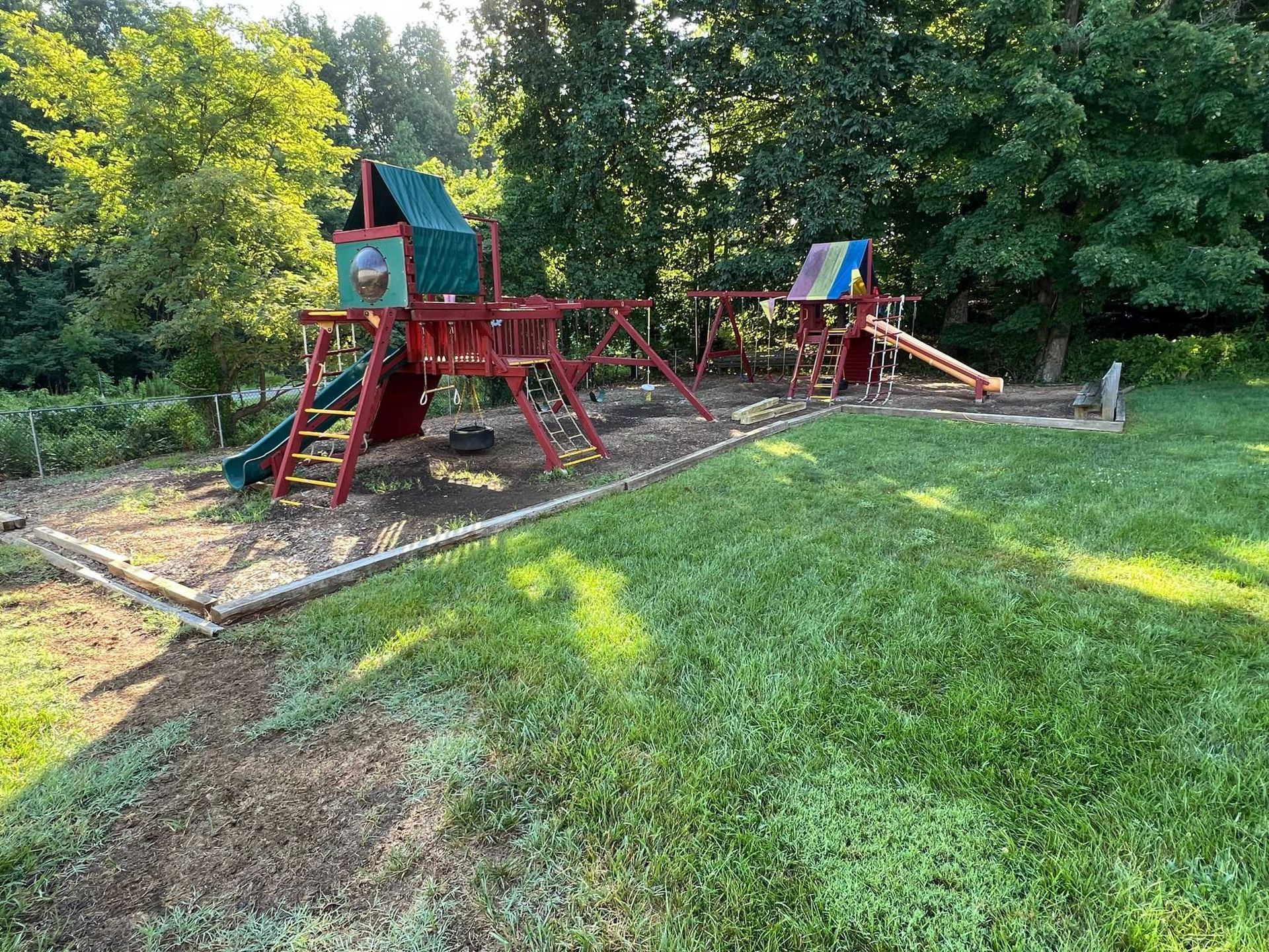 Wooden playground with red climbing frame and slide beside a grassy lawn and trees