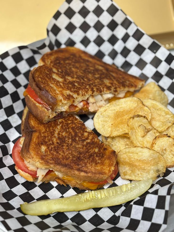 Grilled sandwich with chips and a pickle on checkered paper-lined tray