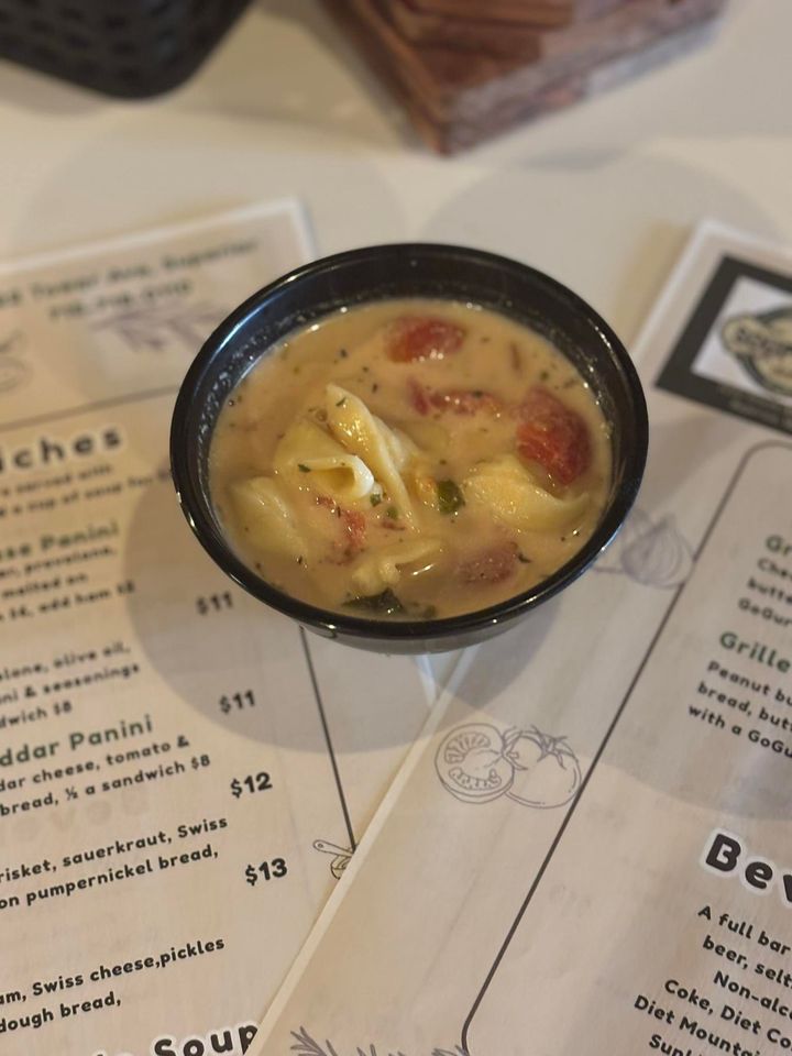 Small bowl of creamy soup on a restaurant menu, with visible tomato and vegetable pieces.