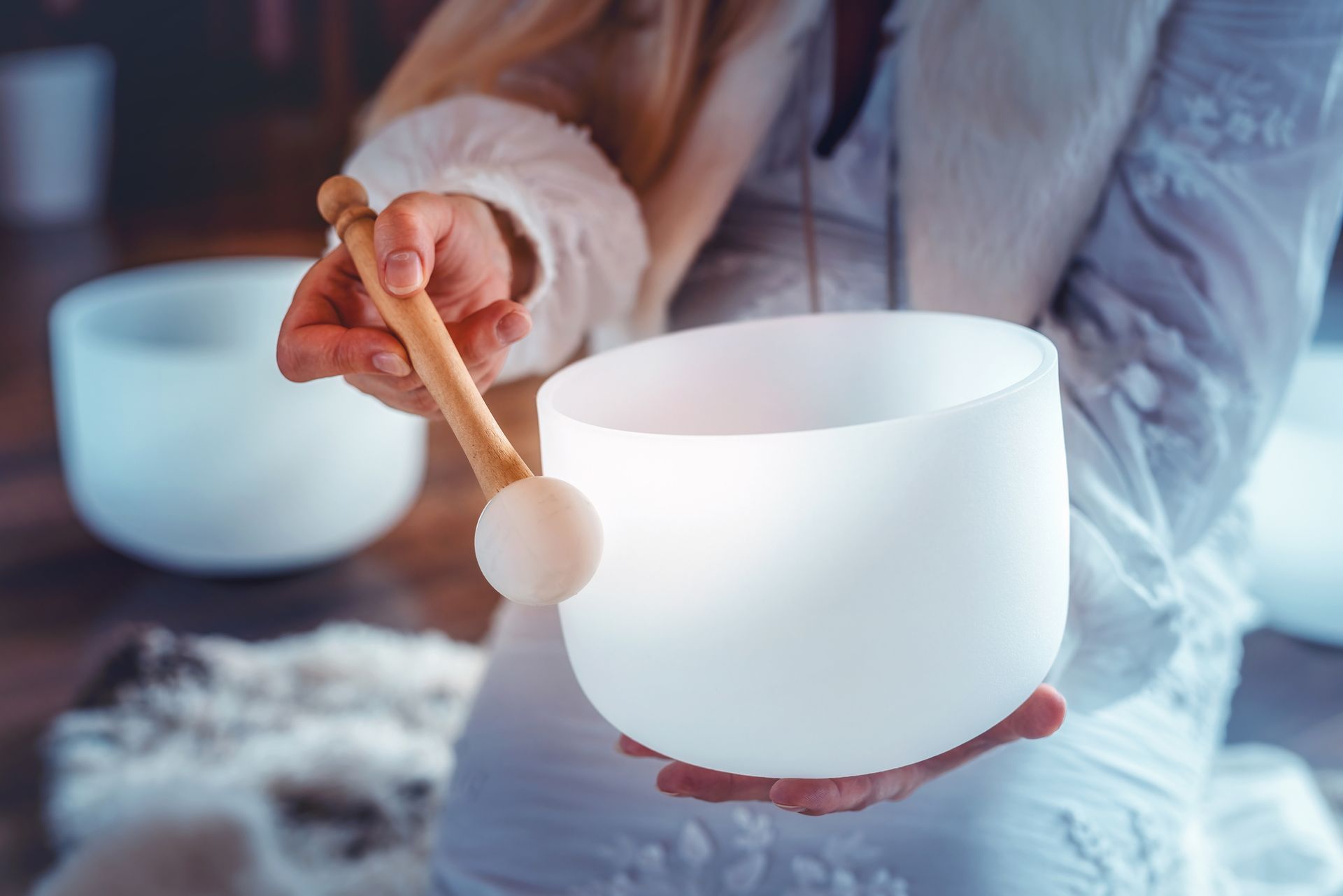 A woman is holding a singing bowl with a wooden stick in her hands.