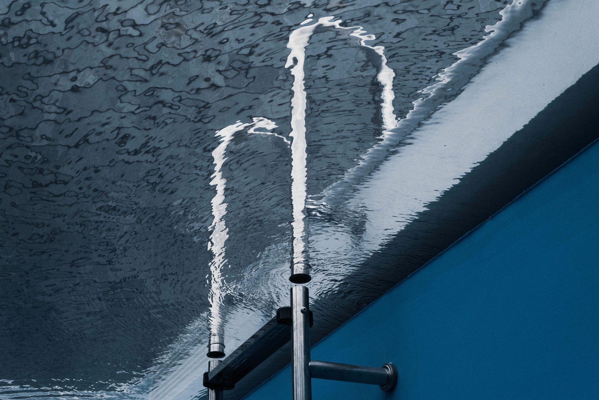 A stainless steel ladder mounted on a blue wall. Water runs down the side of the wall and ladder.