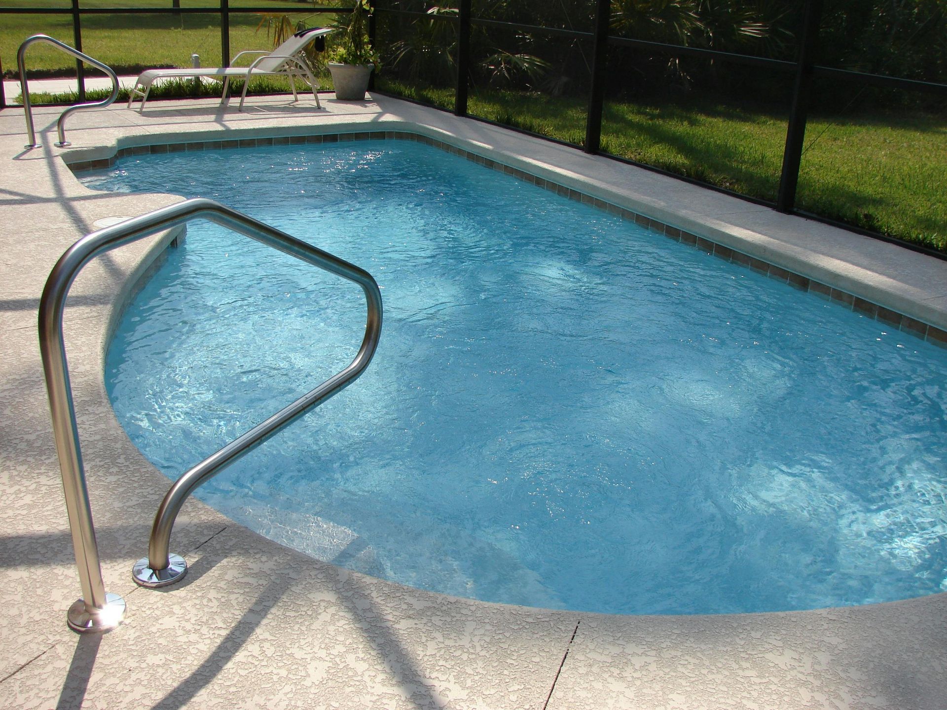 Small backyard pool with a curved edge, handrail, and clear blue water.