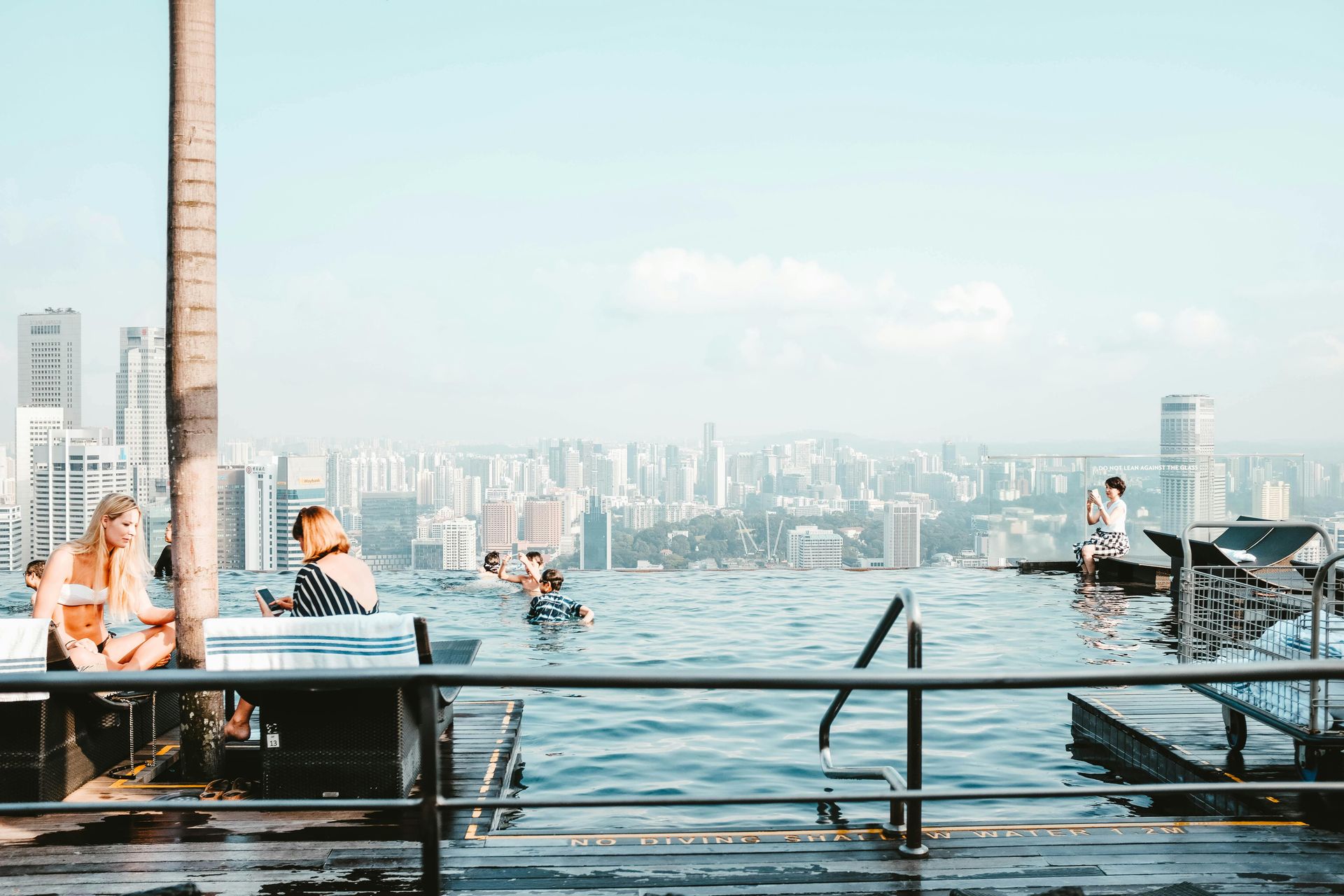 Infinity pool overlooking a cityscape; people swimming and relaxing under a bright sky.