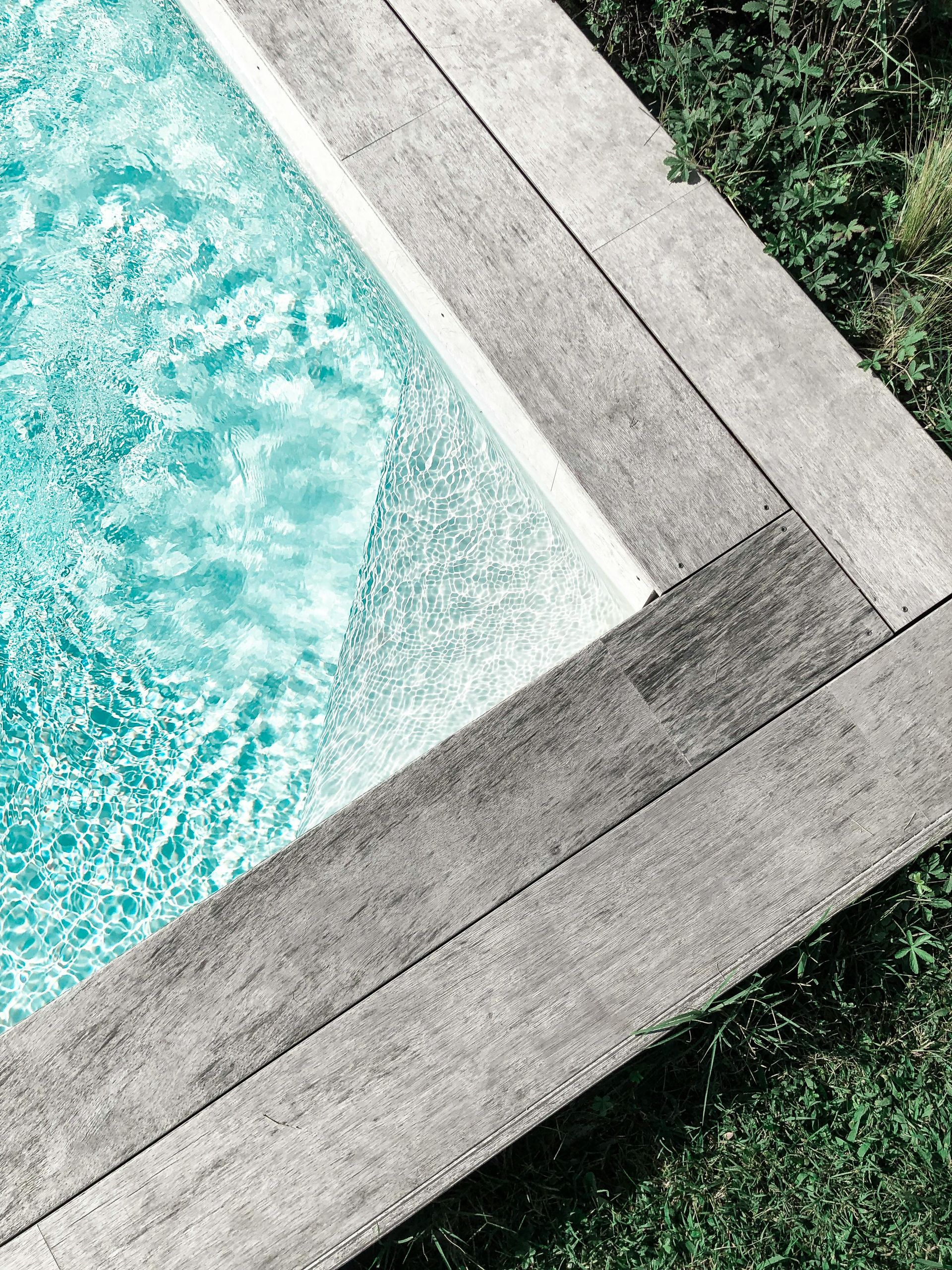 Pool with turquoise water surrounded by a gray concrete border and green grass.