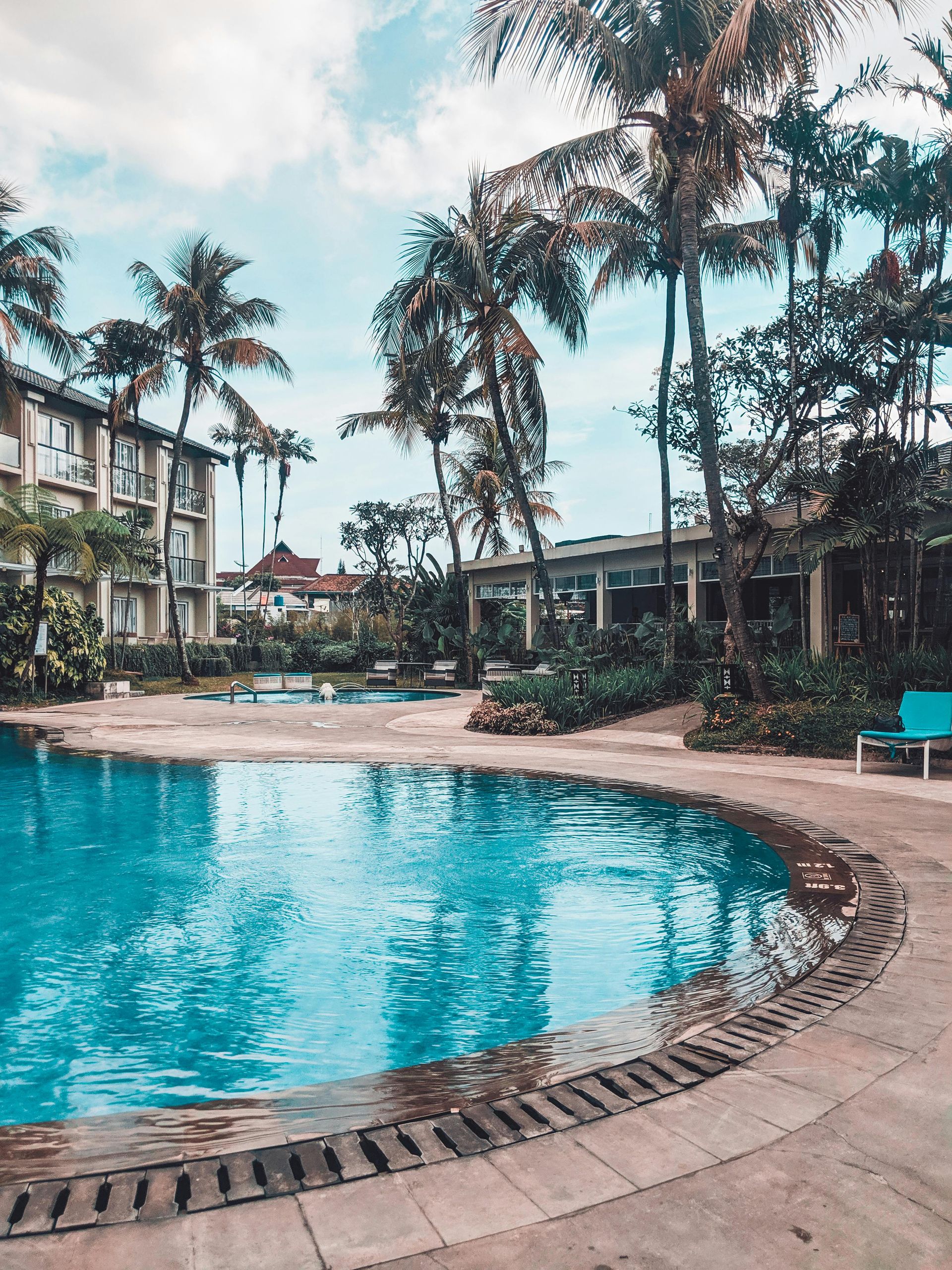 Swimming pool with blue water surrounded by palm trees and a hotel.
