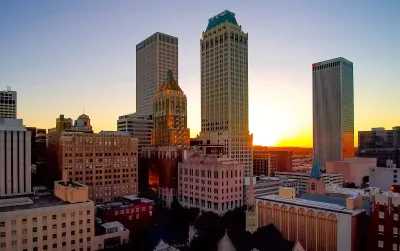 Sunset over the downtown Tulsa, Oklahoma skyline, featuring Art Deco skyscrapers and surrounding city buildings.