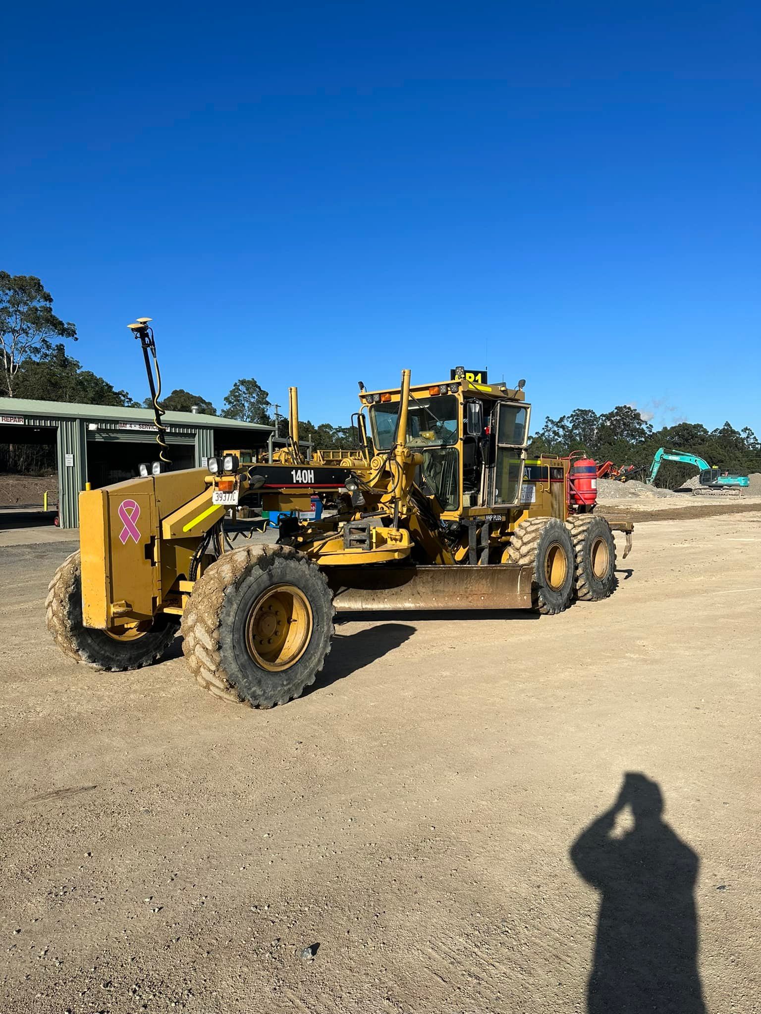 Yellow Caterpillar Grader on Gravel, Under a Blue Sky, With a Person in the Cab — HOLESHOT Diesel In Emerald, QLD
