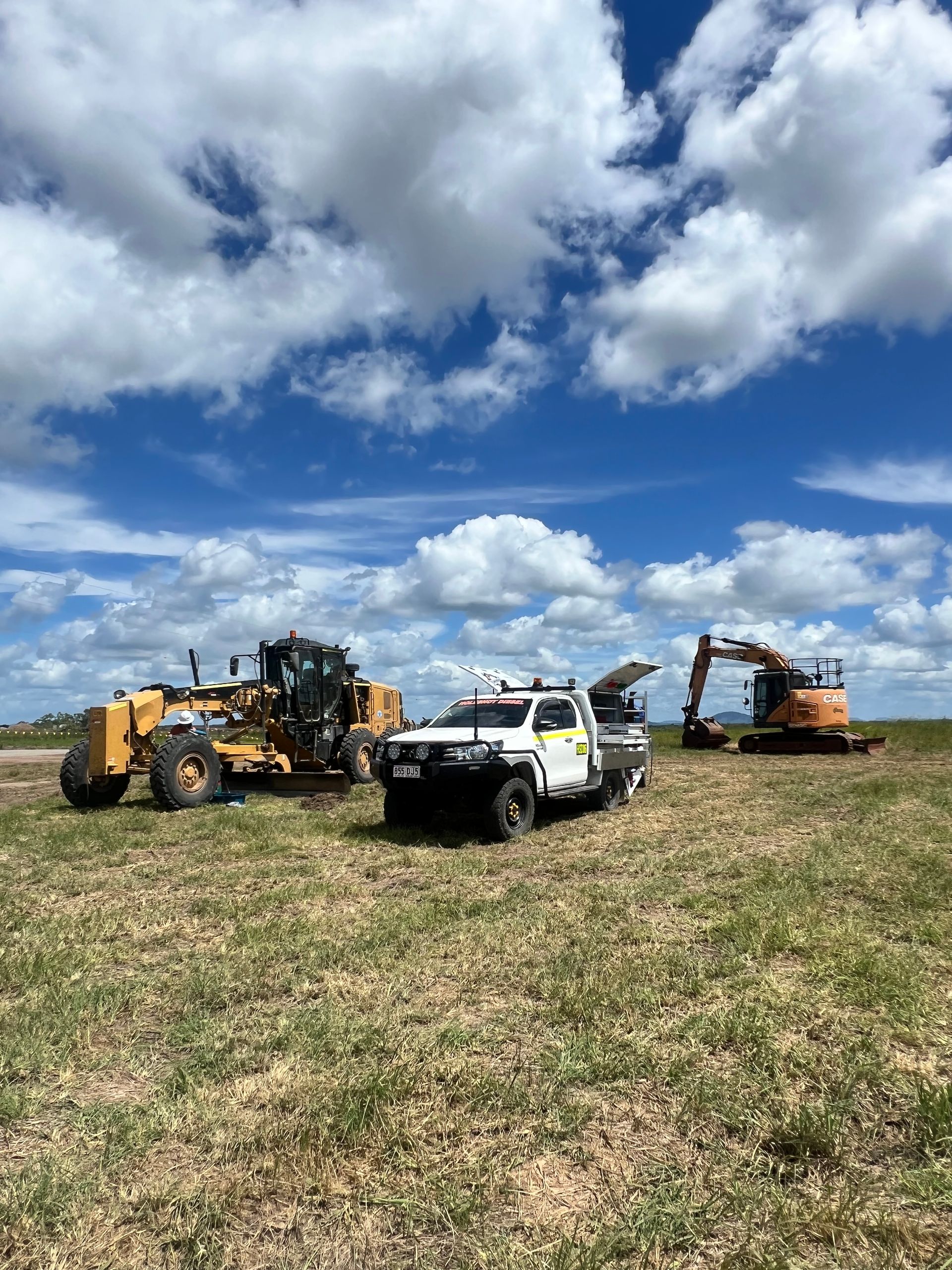 Construction Vehicles on a Grassy Field Under a Cloudy Blue Sky — HOLESHOT Diesel In Rockhampton, QLD