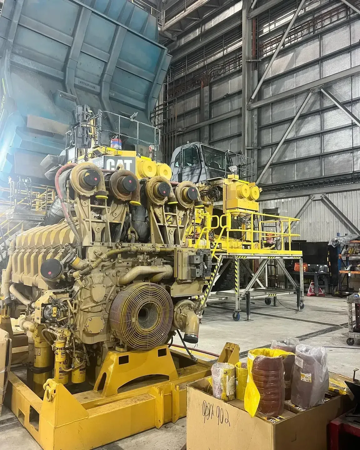 A yellow Caterpillar industrial engine sits on a metal stand inside a large, high-ceilinged industrial workshop.