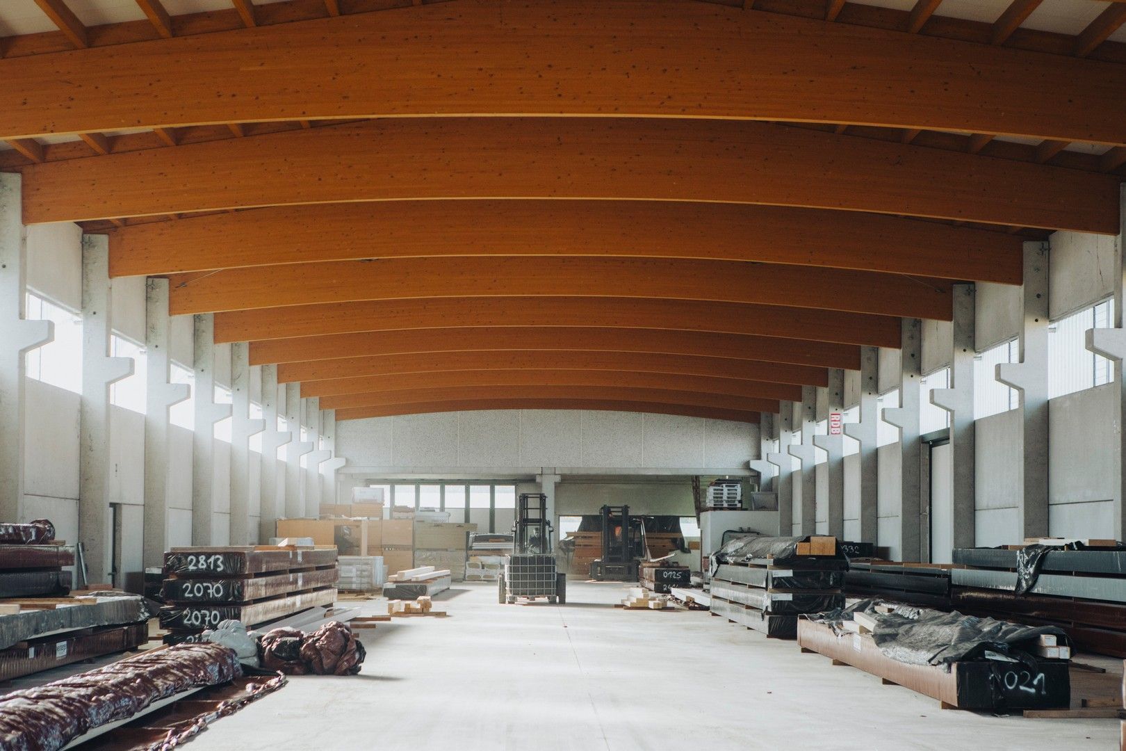 Interno di un grande magazzino con soffitto con travi in legno e supporti in cemento. Materiali da costruzione visibili sul pavimento.