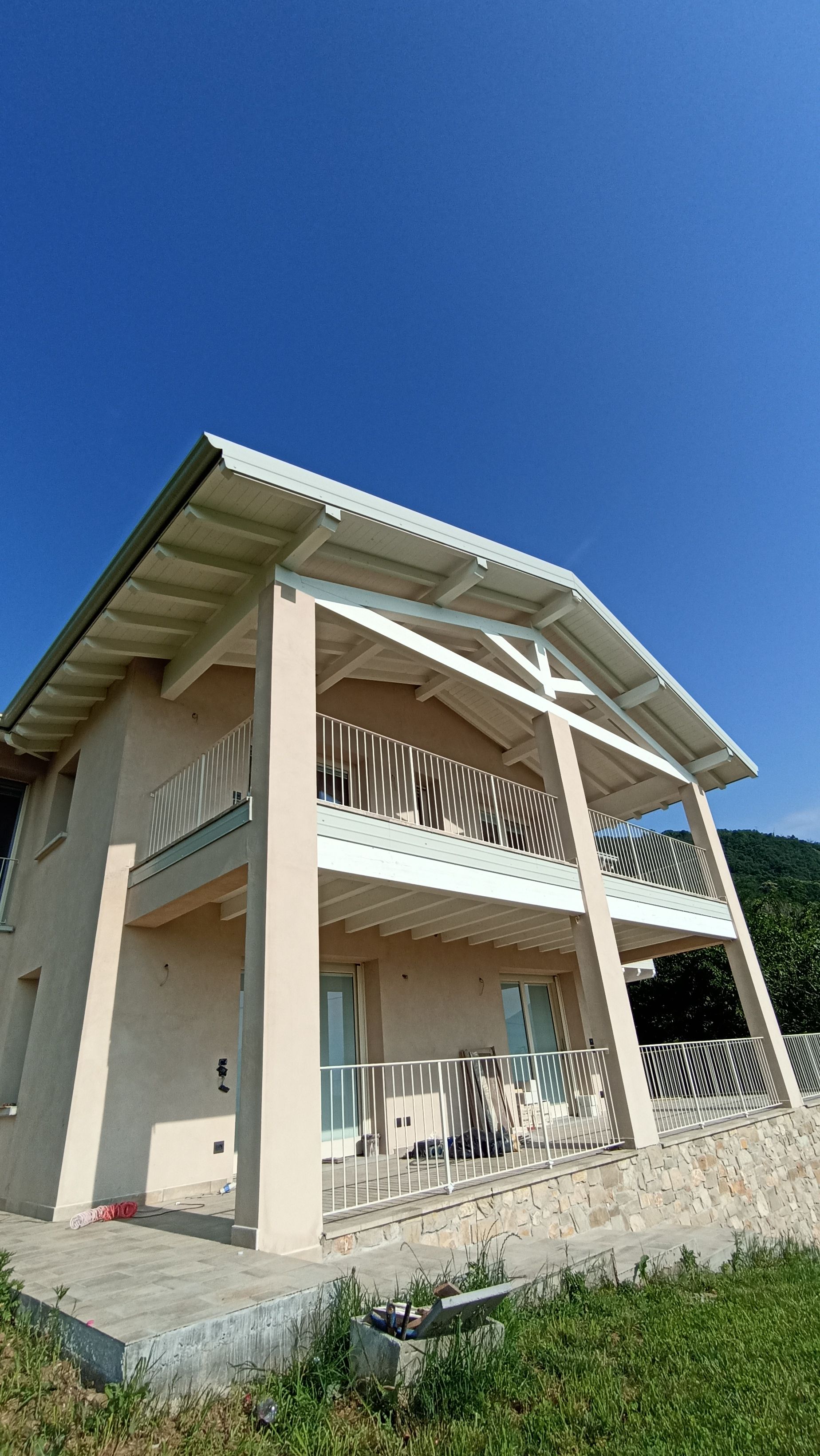 Casa beige a due piani con finiture e balconi bianchi, sotto un cielo azzurro brillante.