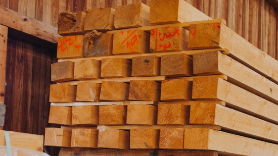 Catasta di legname squadrato all'interno di un edificio in legno, alcuni con segni arancioni.