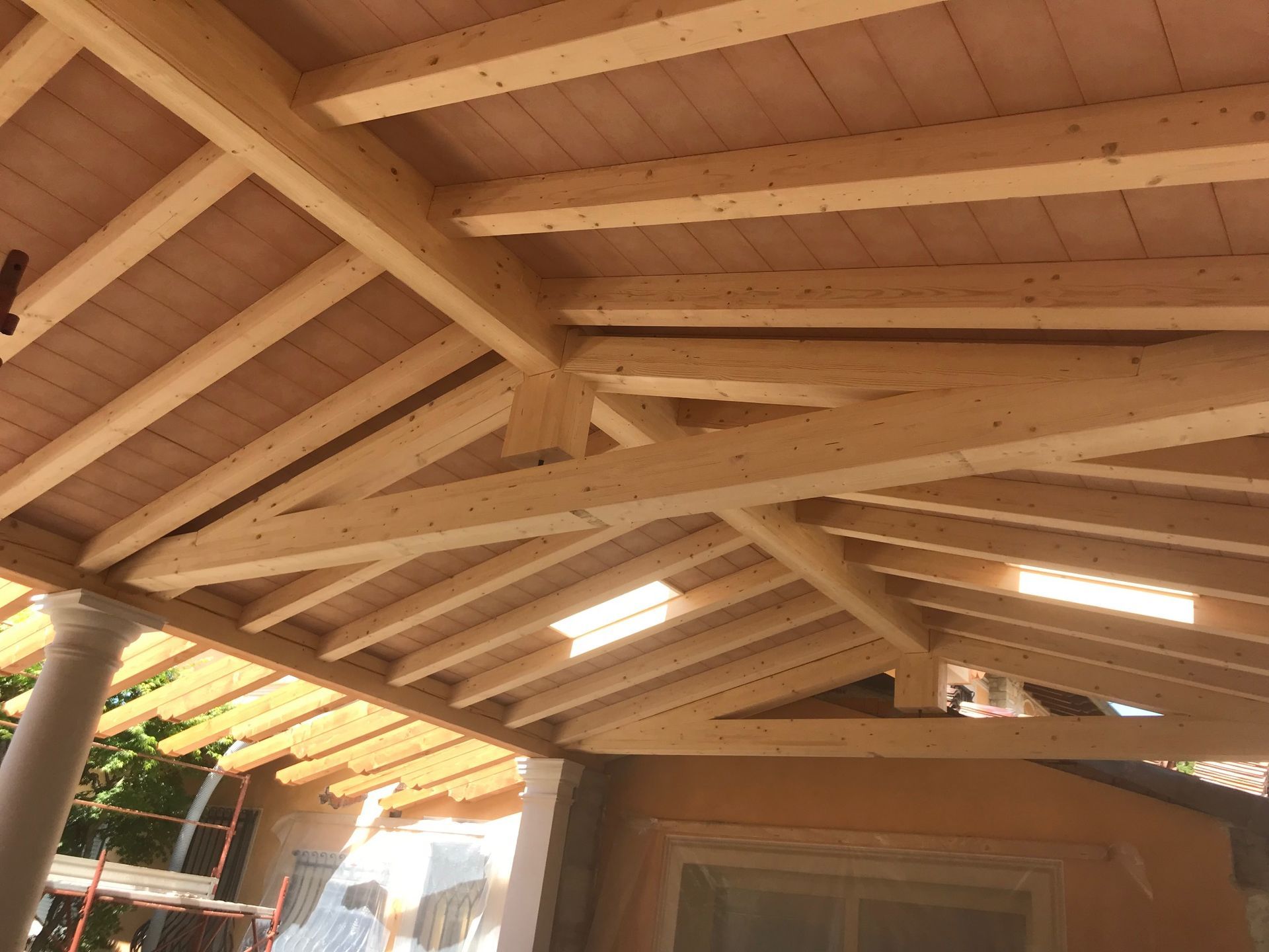Travi e travi in legno che formano la struttura del tetto, con un soffitto e pilastri color marrone chiaro visibili.
