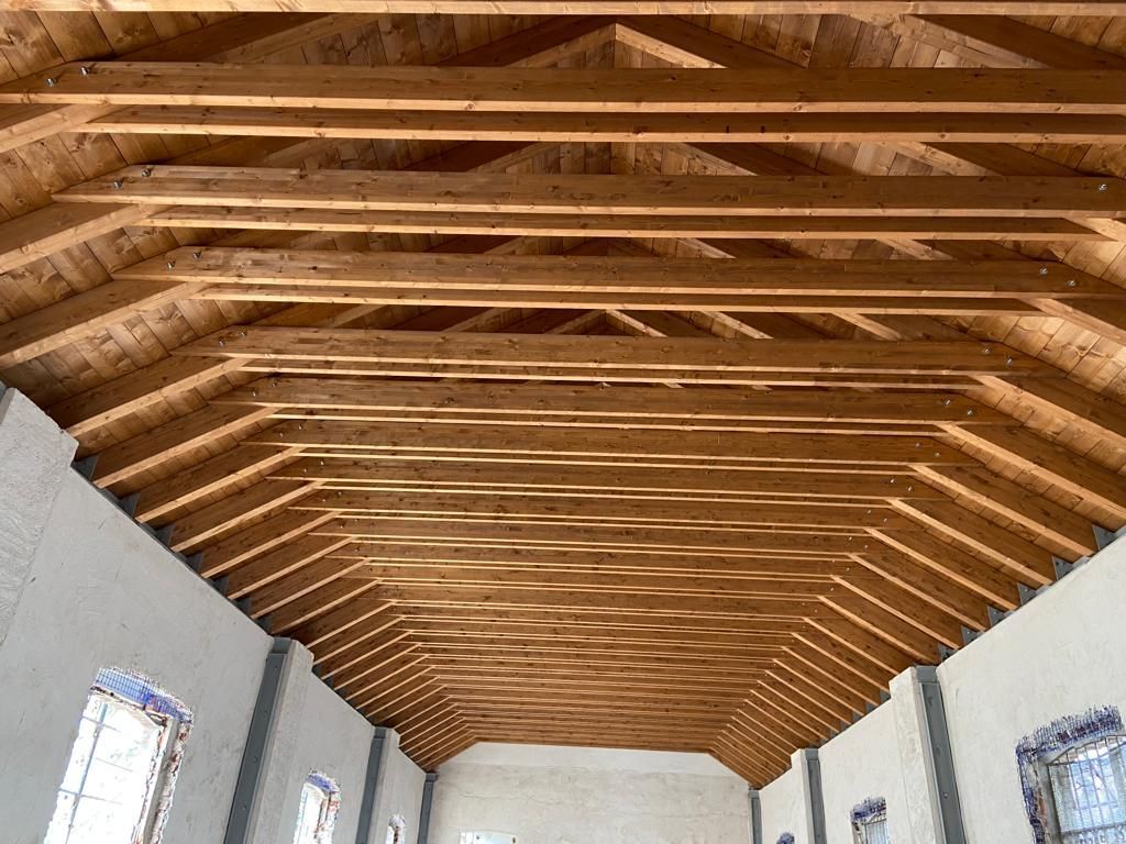 Travi in legno sul soffitto in una stanza luminosa con pareti e finestre bianche.