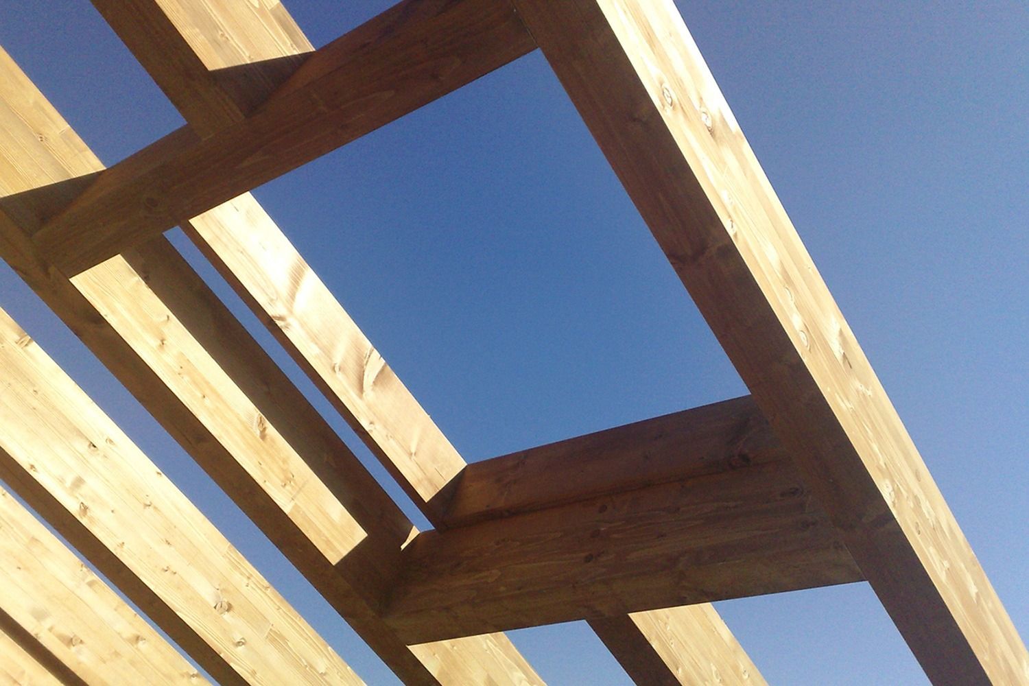 Travi di legno che formano un'apertura rettangolare contro un cielo azzurro e terso.