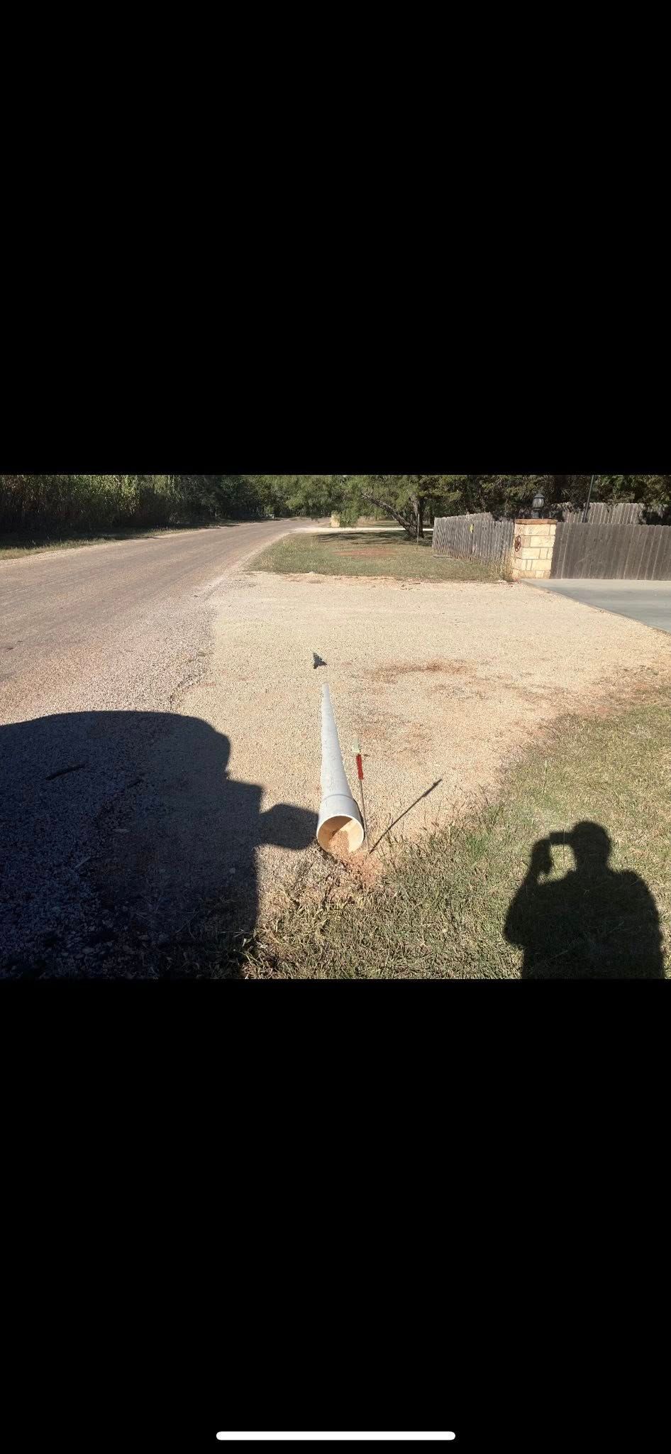 A shadow of a person taking a photo near a gravel driveway and grassy area.