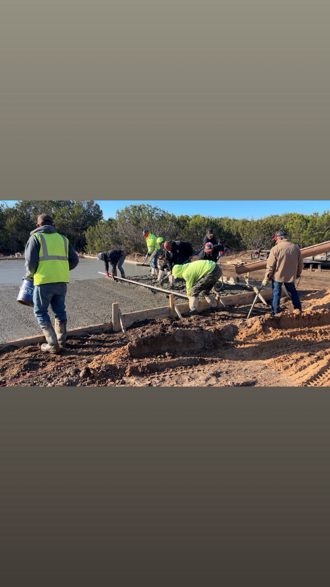 Workers in safety vests and boots on a construction site near water, digging and inspecting.