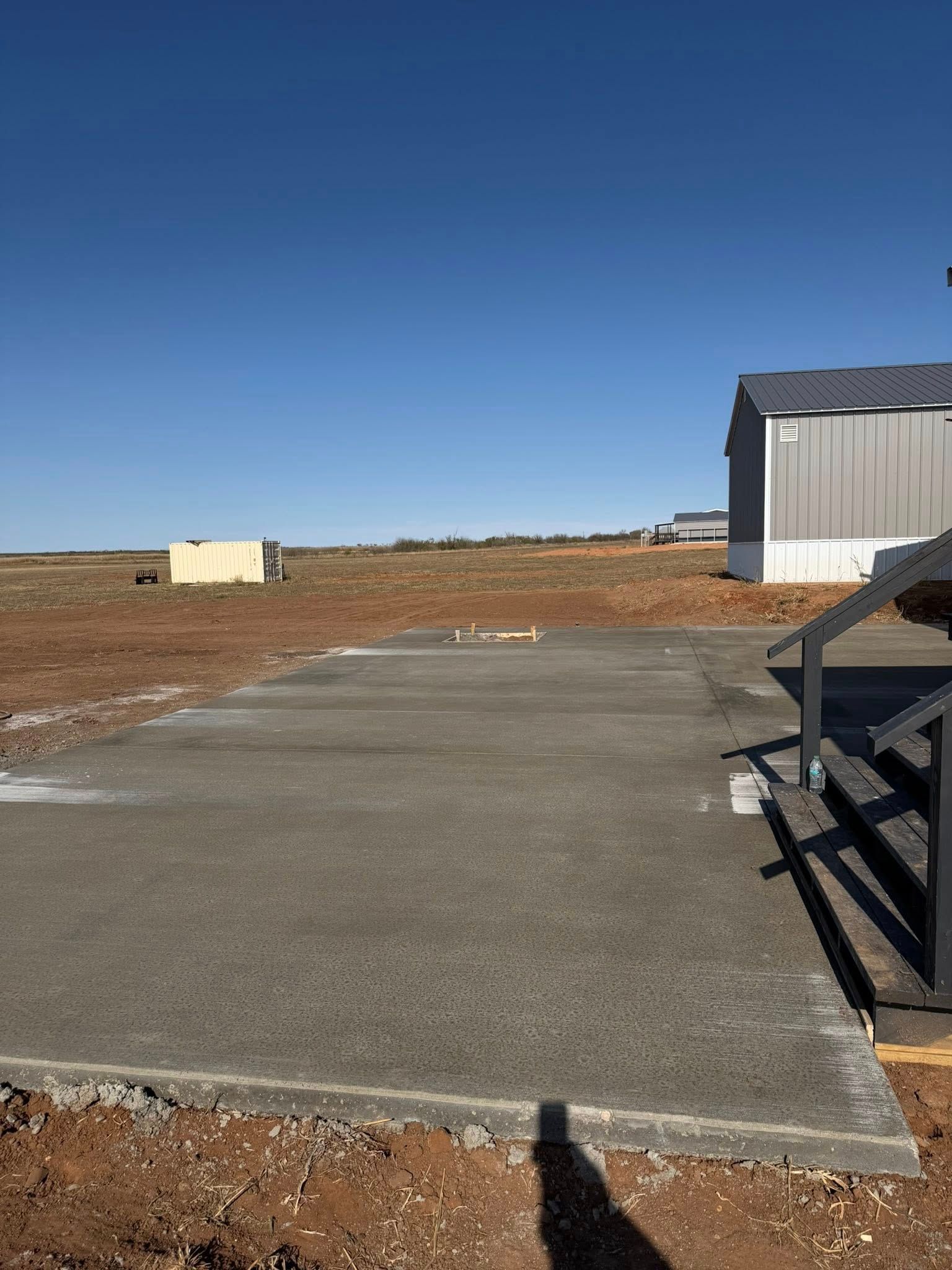 Concrete pad with a small building in the background on a clear, sunny day.