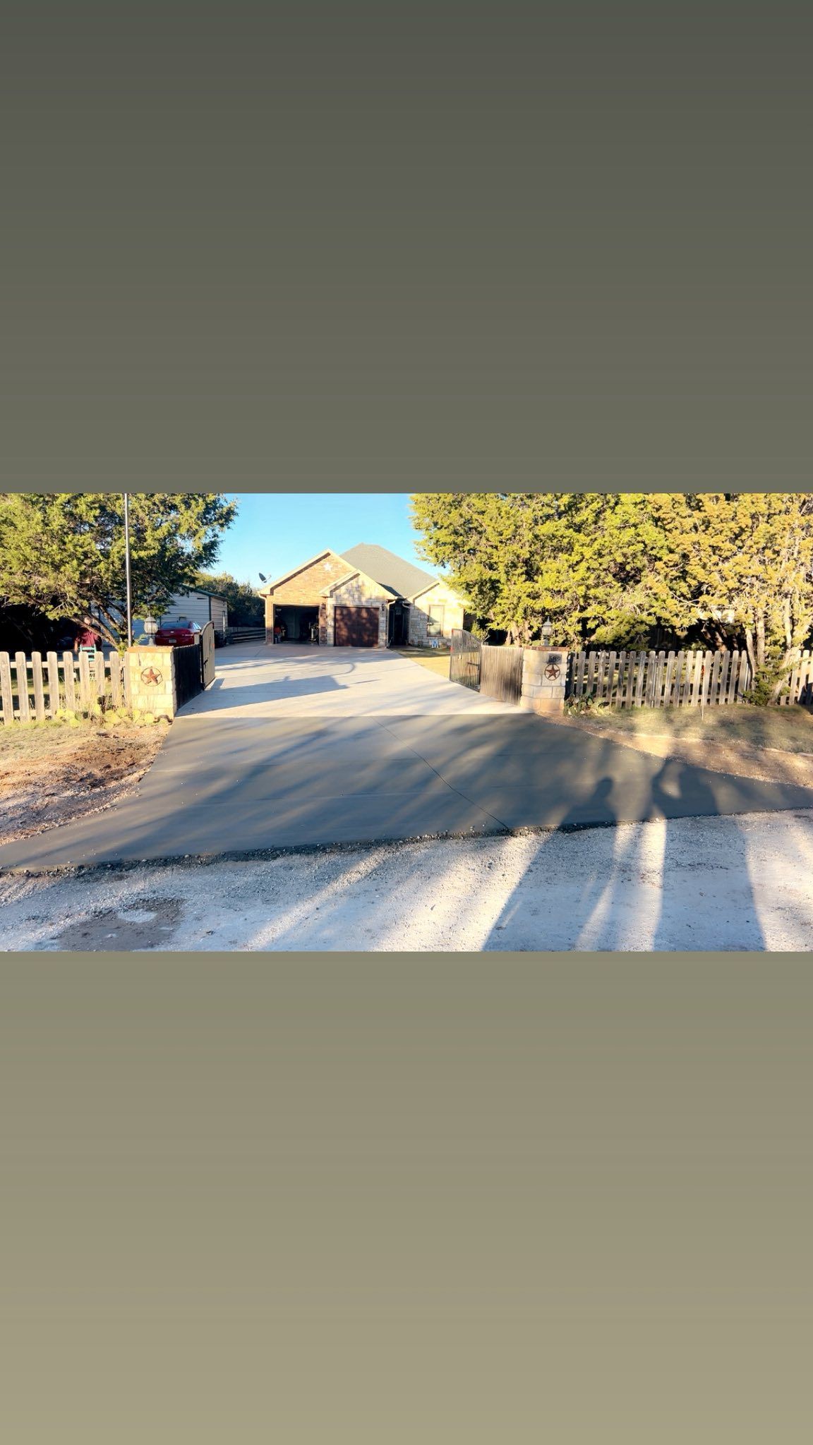 Gravel driveway leads to a light-colored building between trees. Wooden fence on either side.