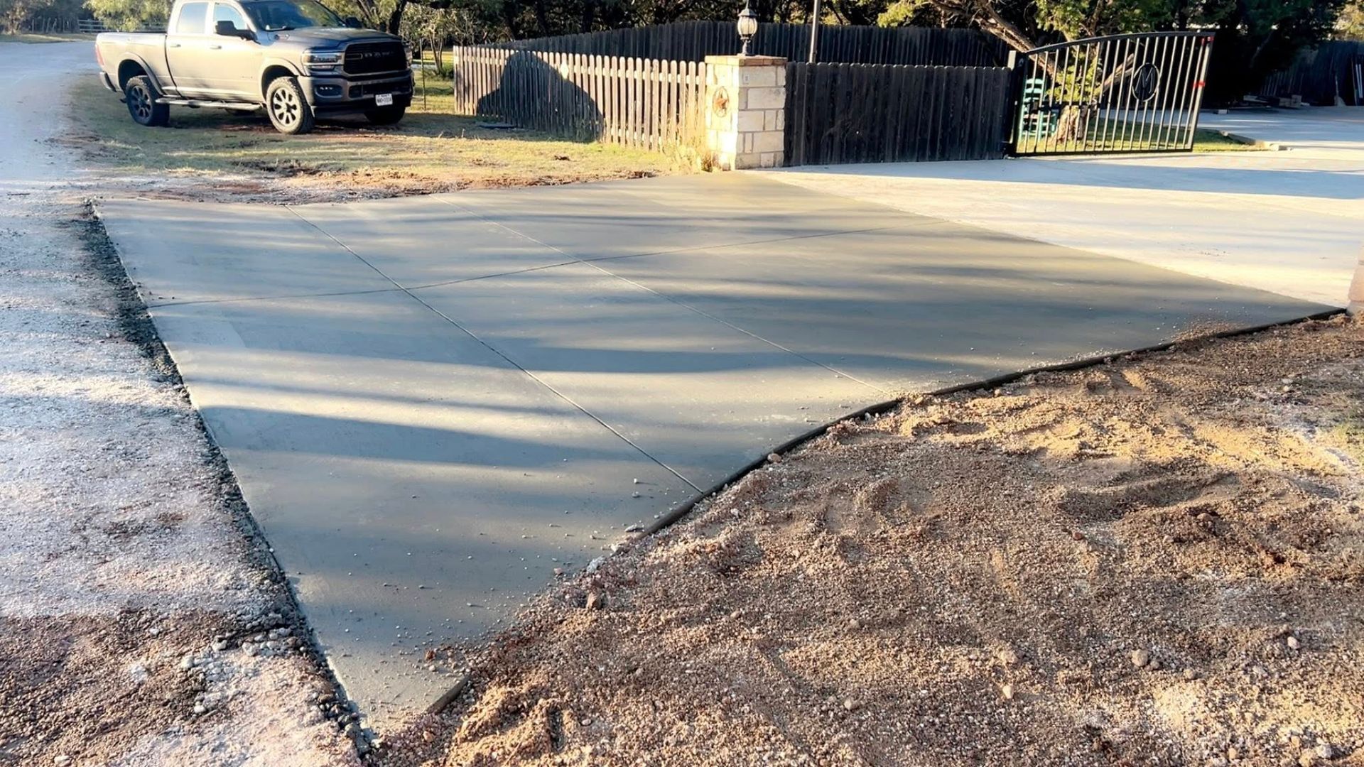 Freshly poured concrete driveway in front of a fence and a truck.