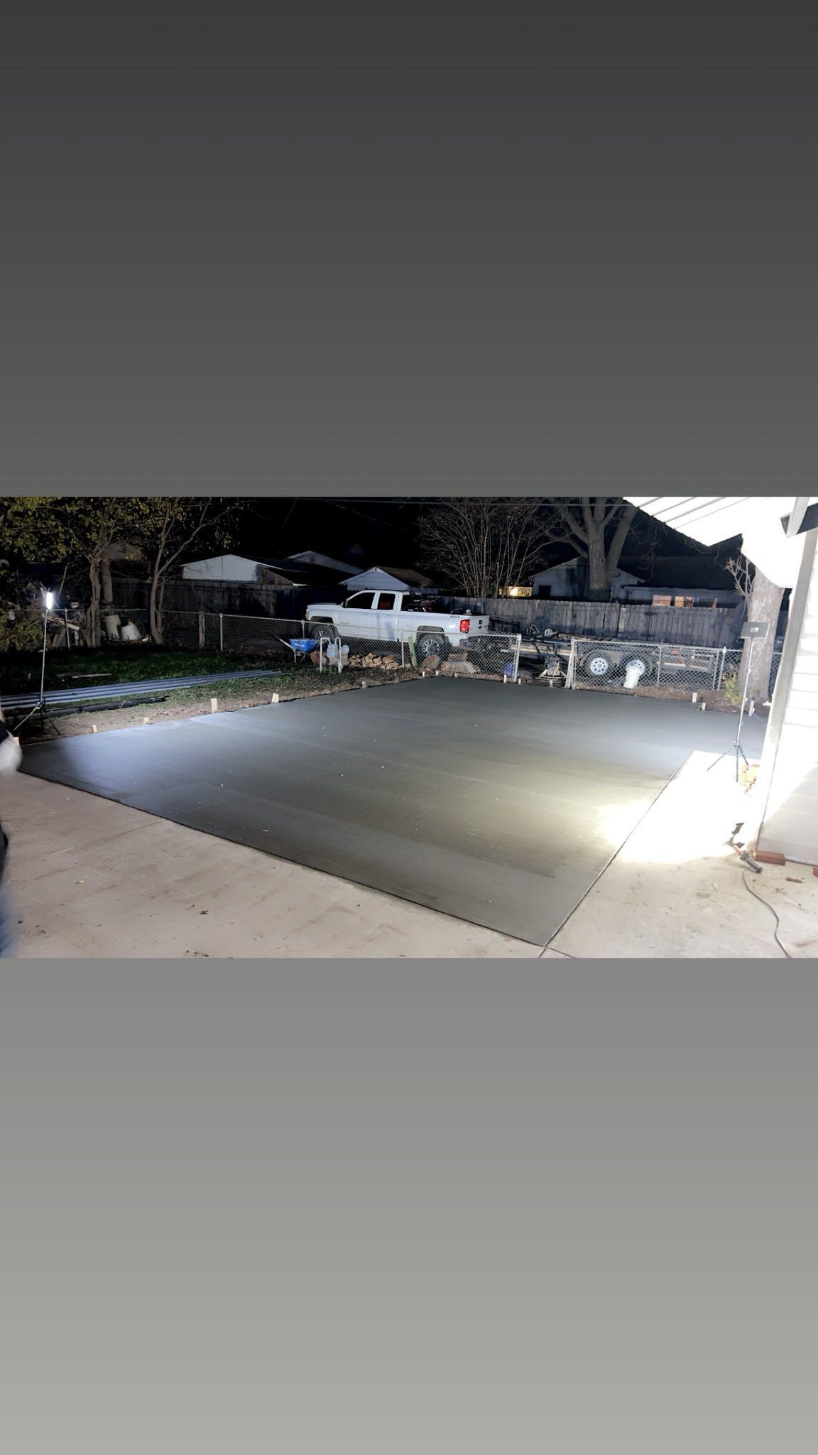 Outdoor scene at night: pool covered with a dark tarp; nearby, houses and trees are visible.