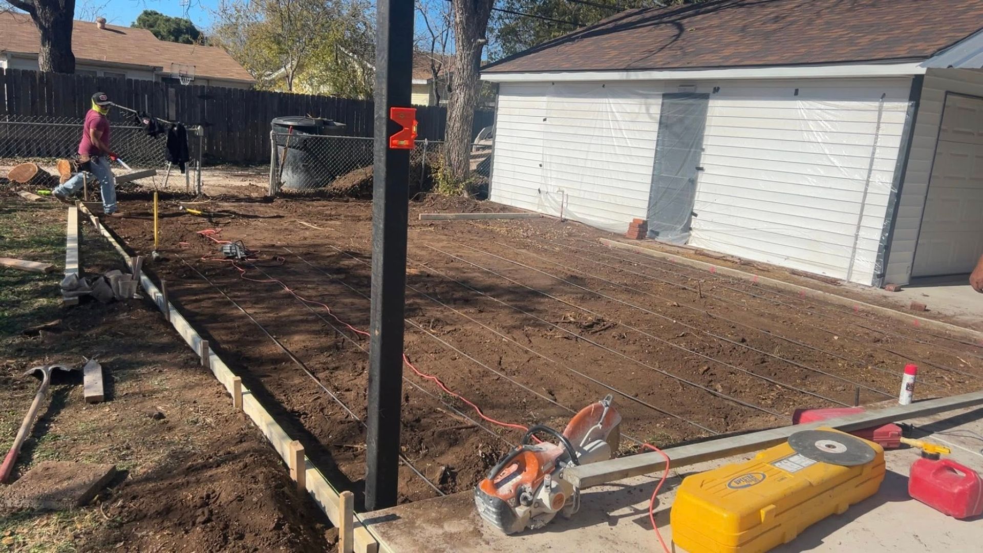 Construction site with freshly graded soil, concrete forms, and equipment. A worker is visible.