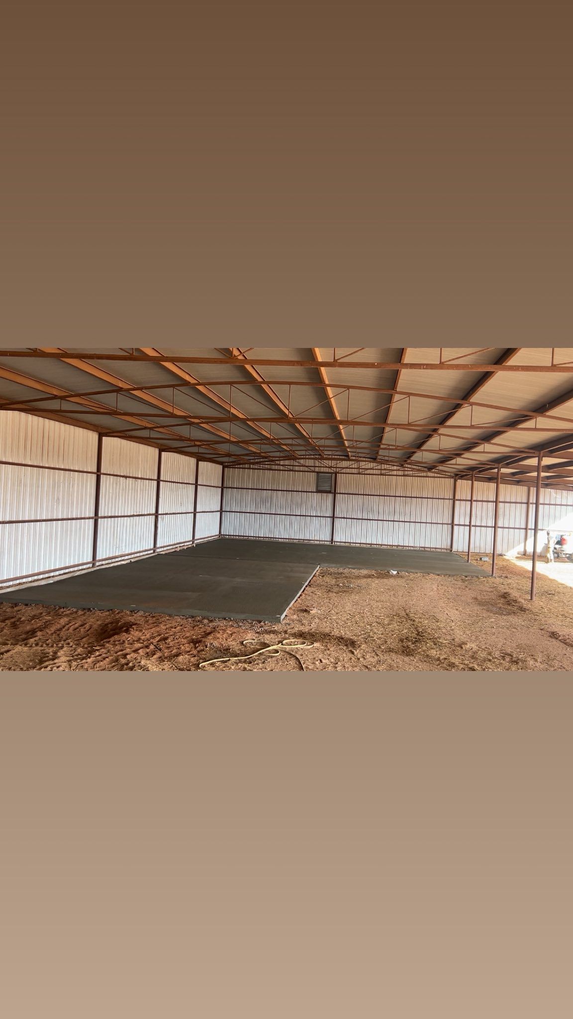Open-sided metal shed with a dirt floor, partially shaded by the roof.
