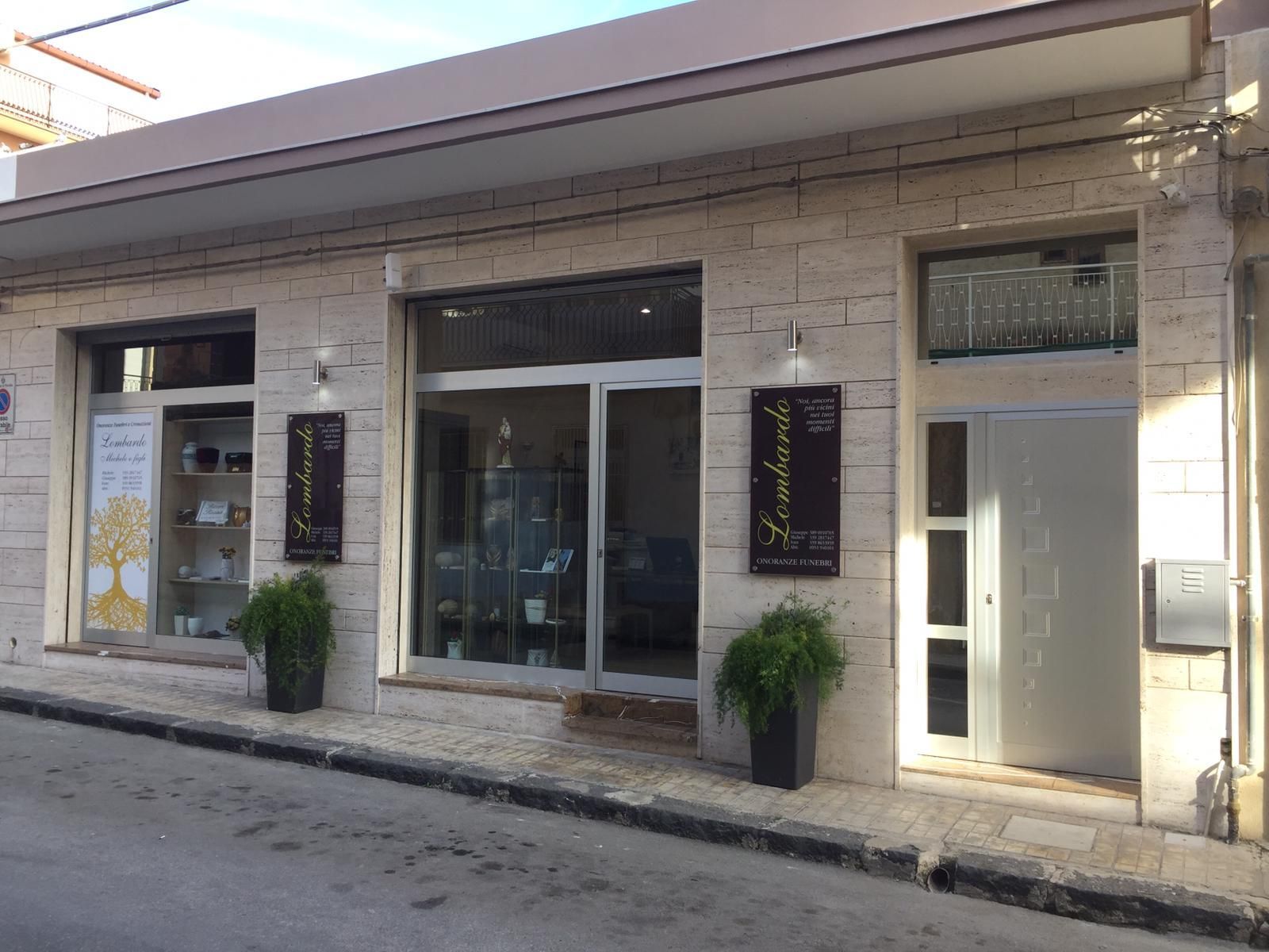 Vetrina con porta e finestre in vetro, piante e insegne in un edificio in mattoni beige.