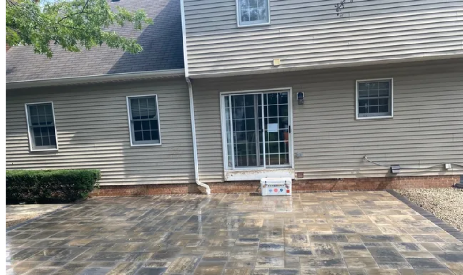 Back patio with gray siding, sliding glass door, and stone paver ground