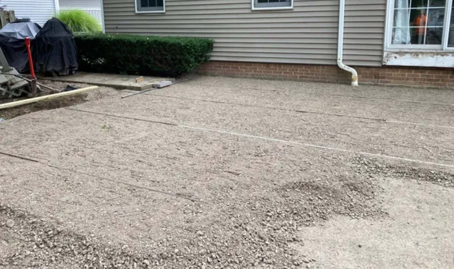 Gravel driveway in front of a beige house with a window, door, and shrubs