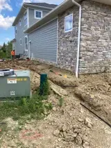 House exterior with exposed dirt trench along the foundation and stone siding under construction