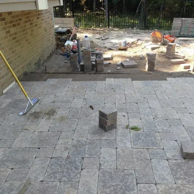 Patio paving stones under construction, with stacked bricks and tools in a backyard