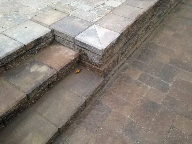 Stone steps beside a tiled walkway with a narrow drainage channel, viewed from above