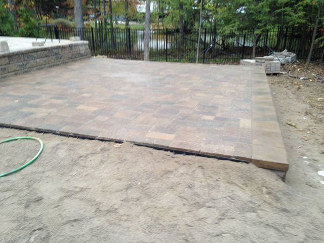 Recently paved patio area with stone pavers, bordered by dirt and a fence, in a yard.