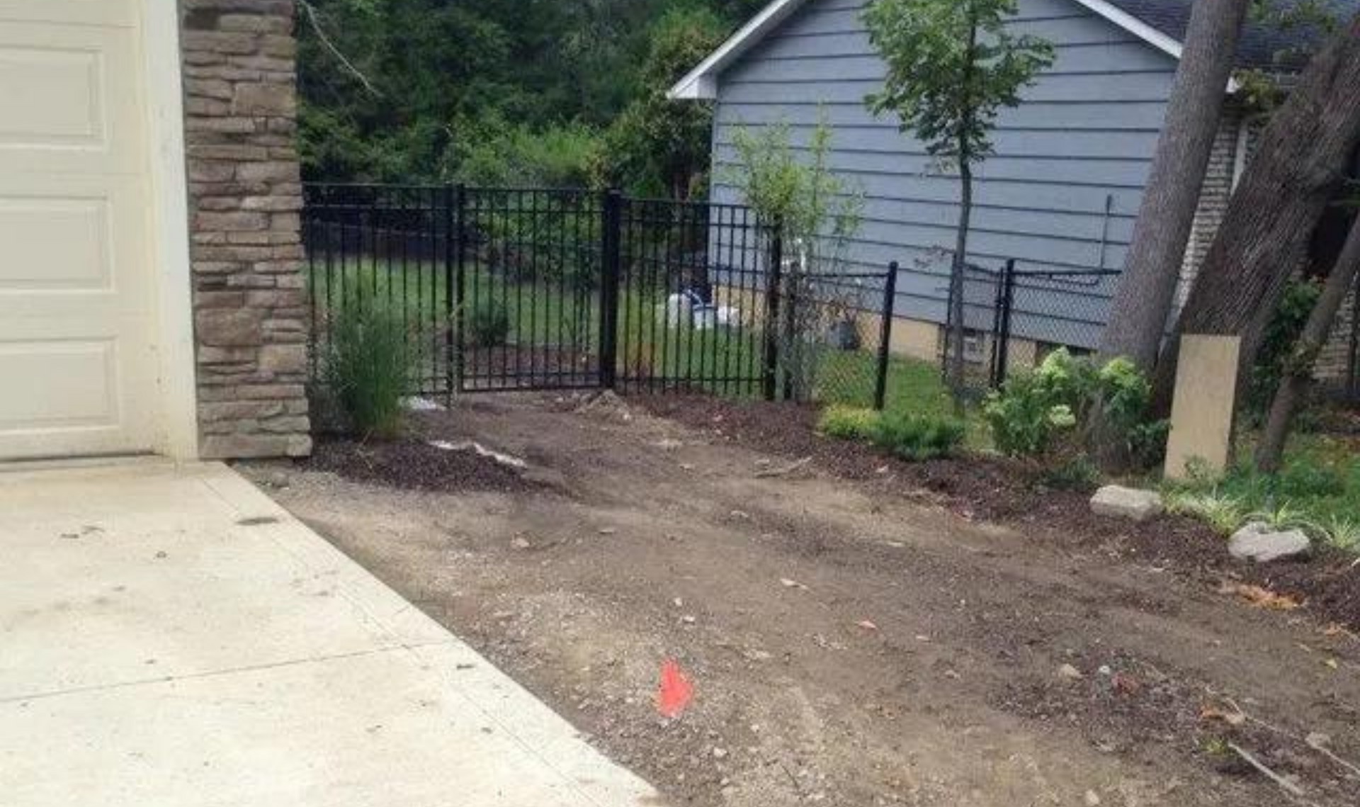 Concrete driveway beside dirt side yard with black fence and gray shed